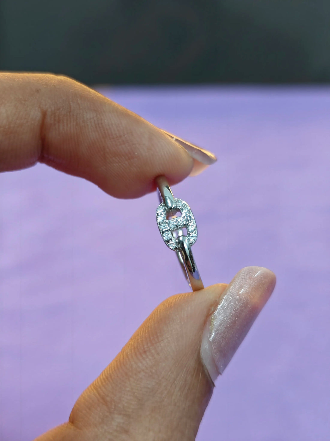 Silver ring with a diamond design held between fingers against a purple background