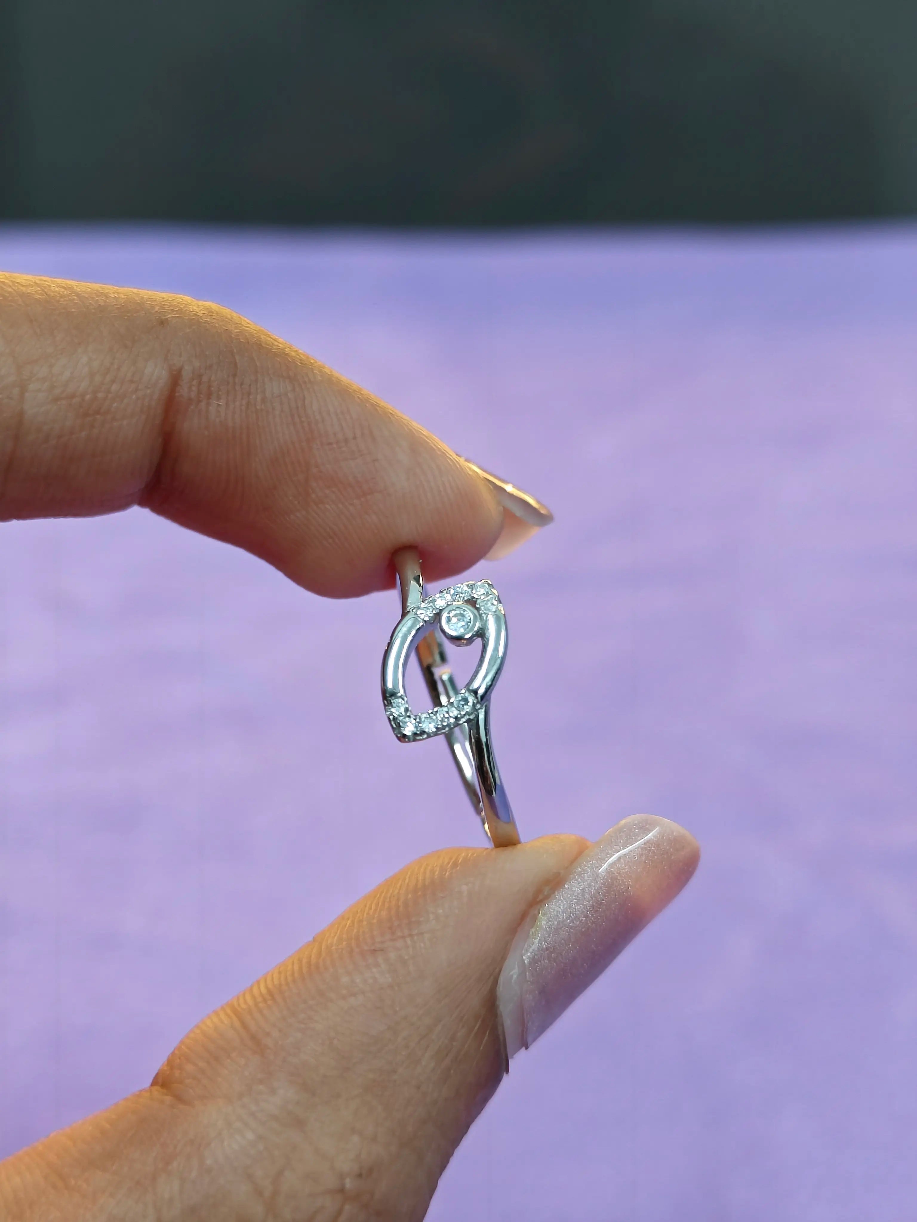 Silver ring with a diamond held between fingers against a blurred purple background