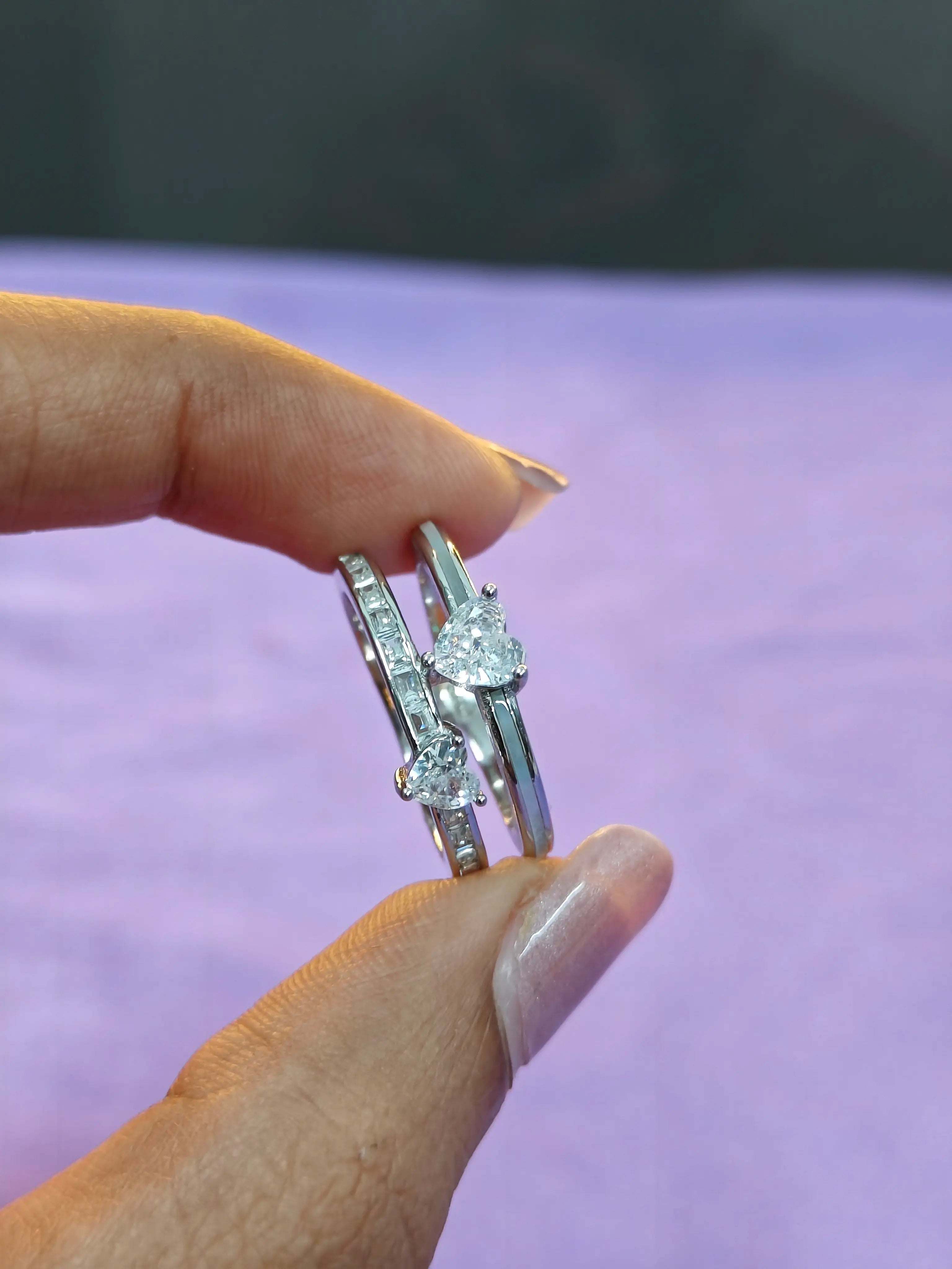 Silver ring with diamond accents held between fingers against a blurred background