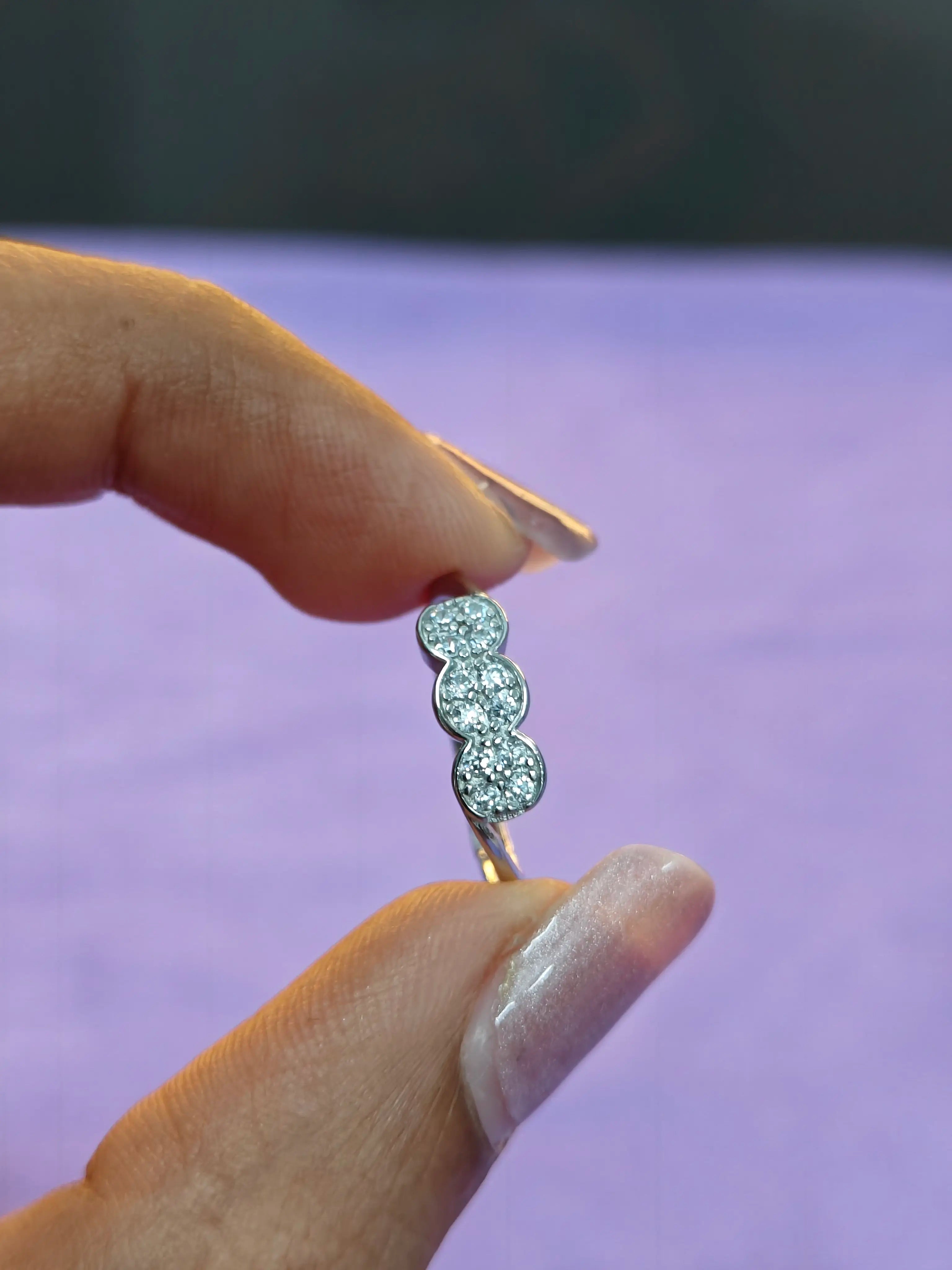 Silver ring with three diamonds held between fingers against a blurred background