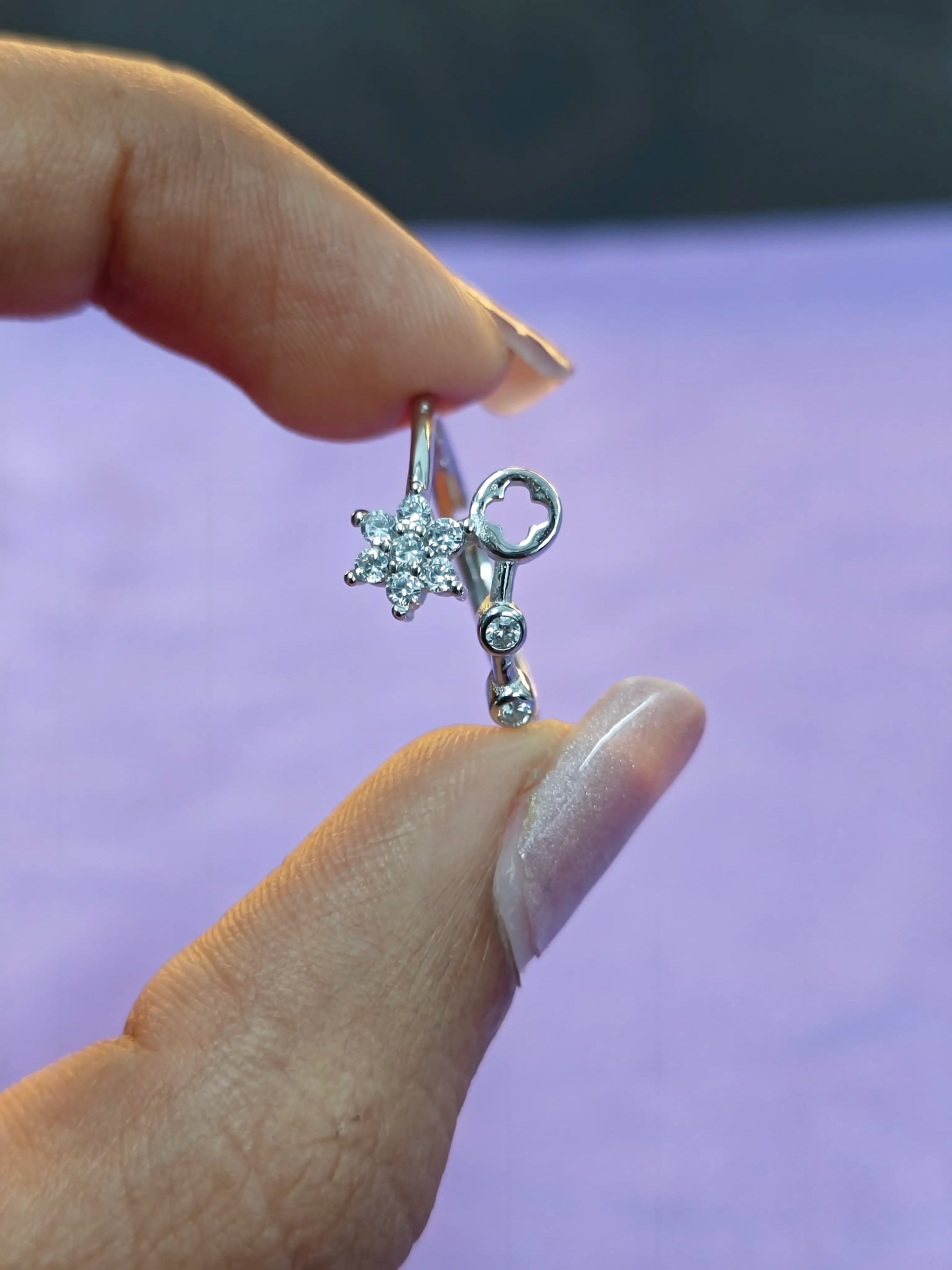 Silver earring with star design held between fingers against a blurred background