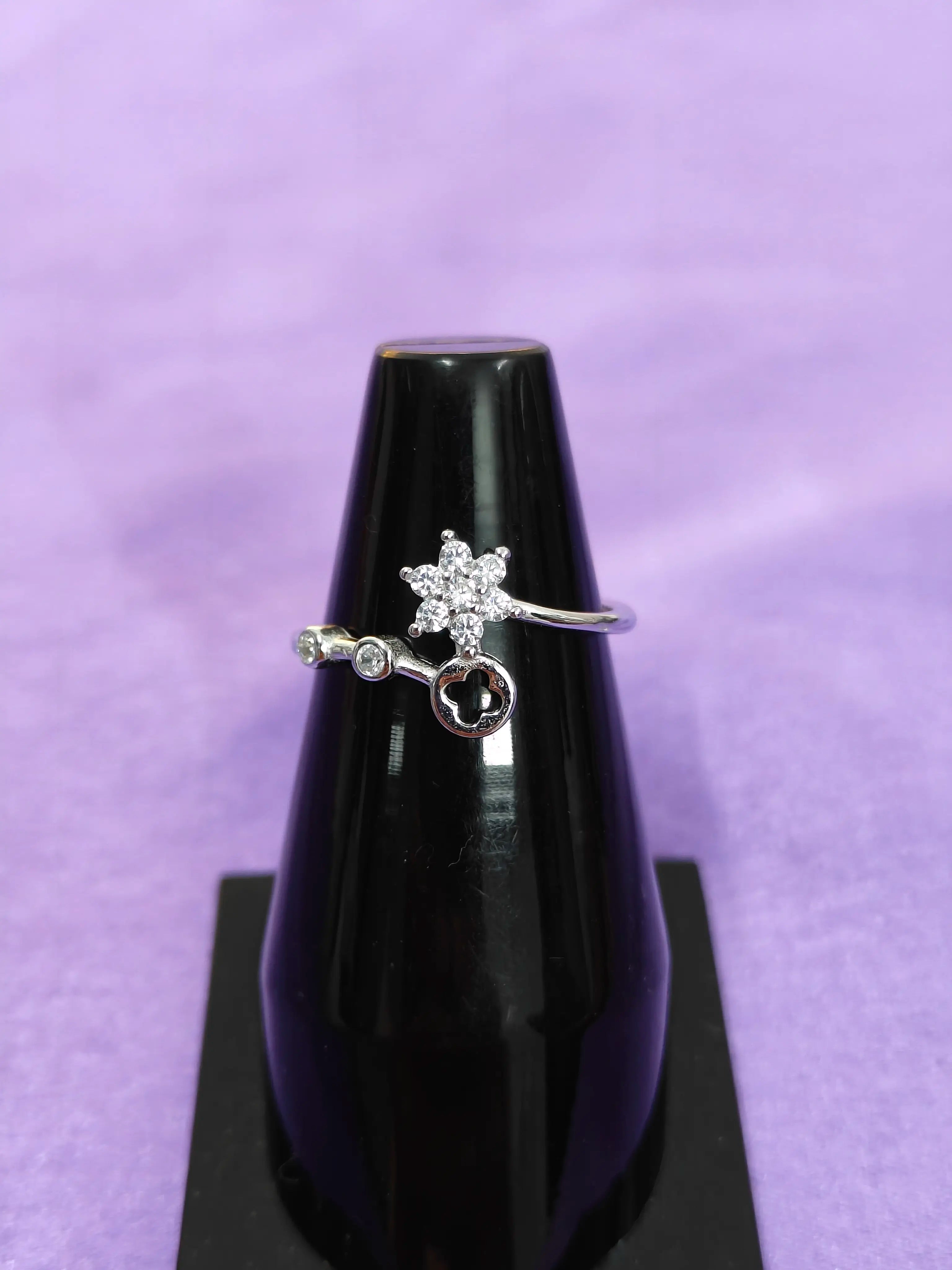 Silver ring with star and key design on a black stand against a purple background