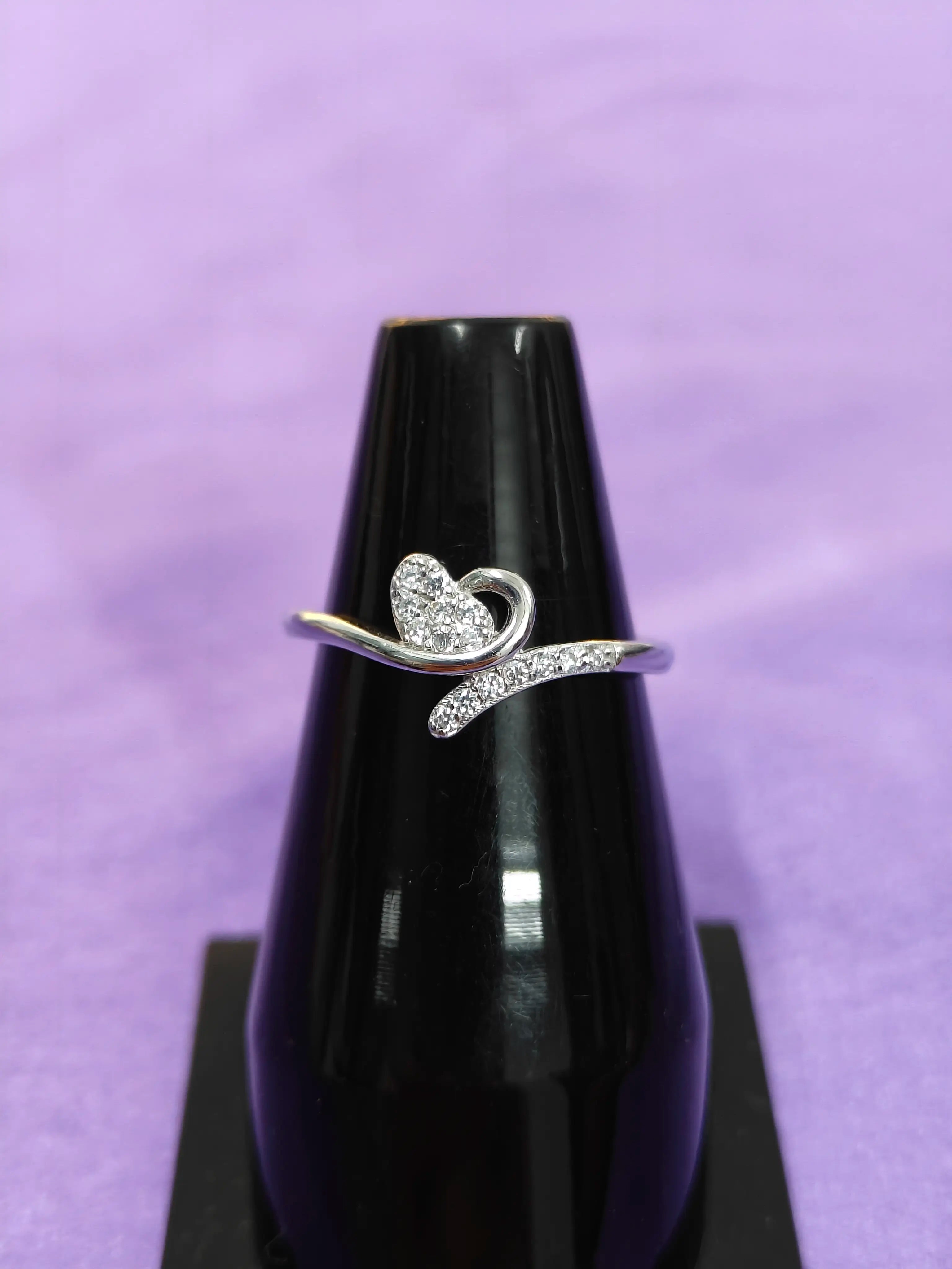 Silver ring with a heart design on a black stand against a purple background