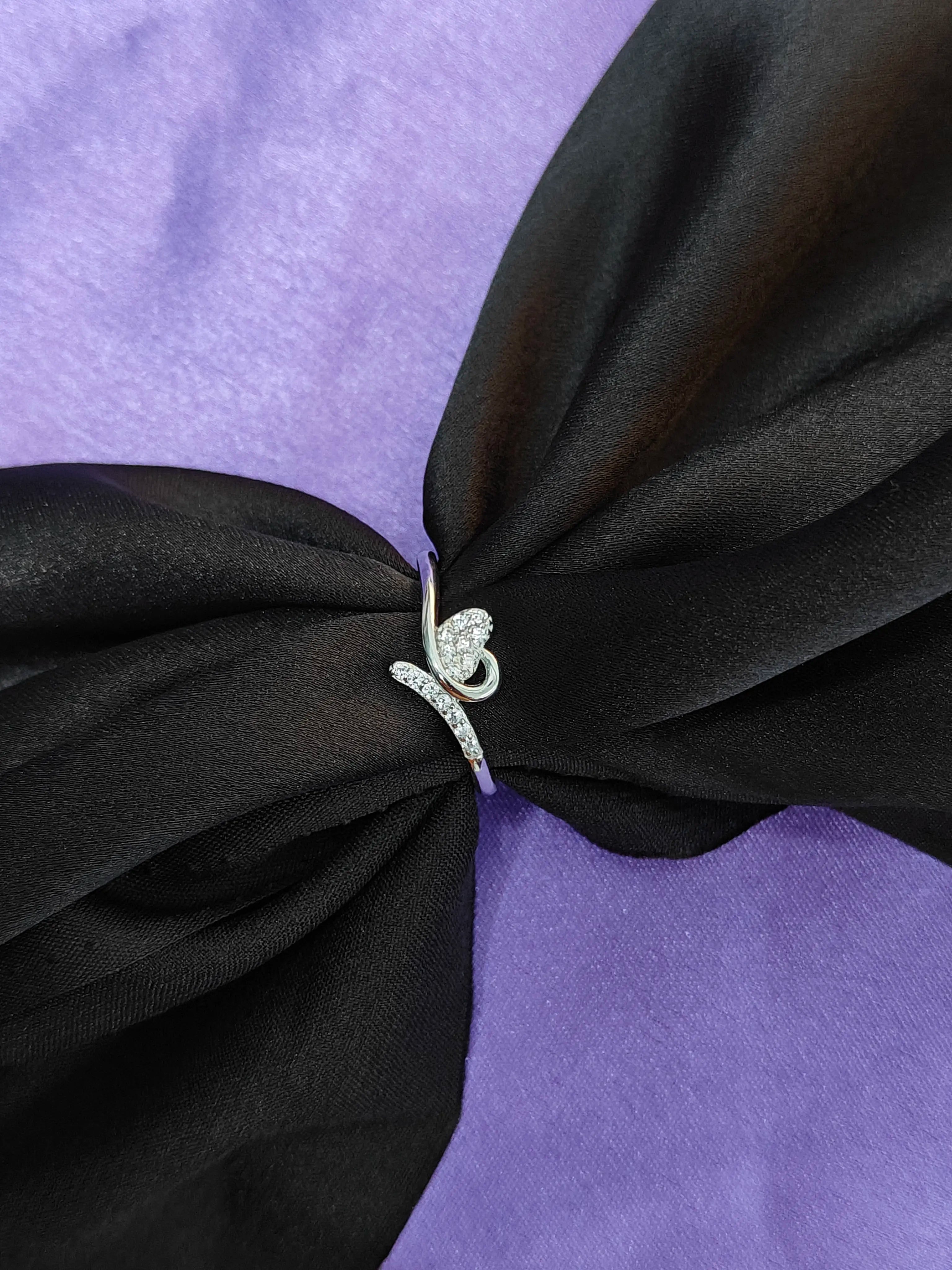 Close-up of a black dress with a purple bow and a silver ring on a matching purple background