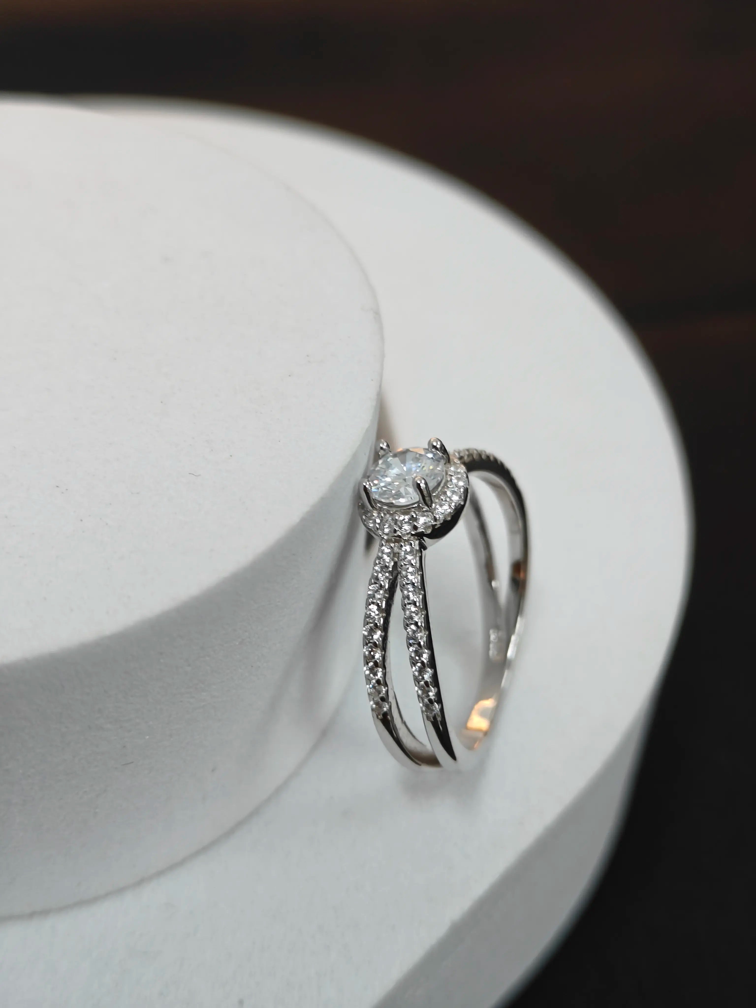 Silver ring with a diamond on a white stand against a dark background