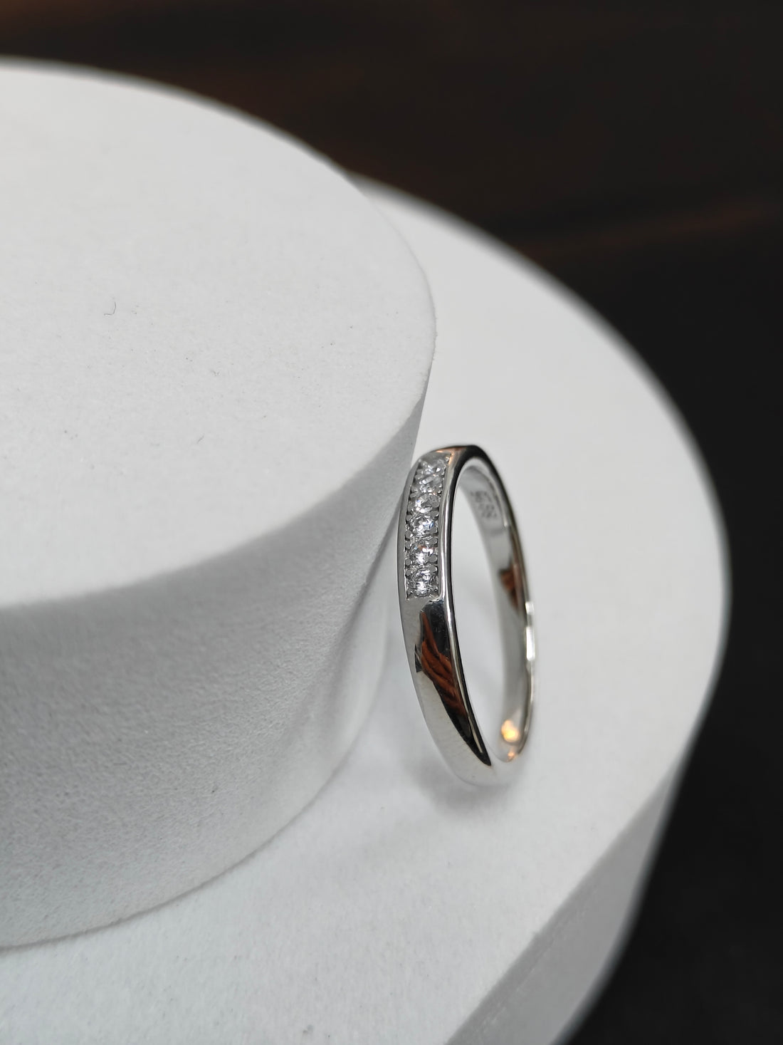 Silver ring with small diamonds on a white stand against a dark background