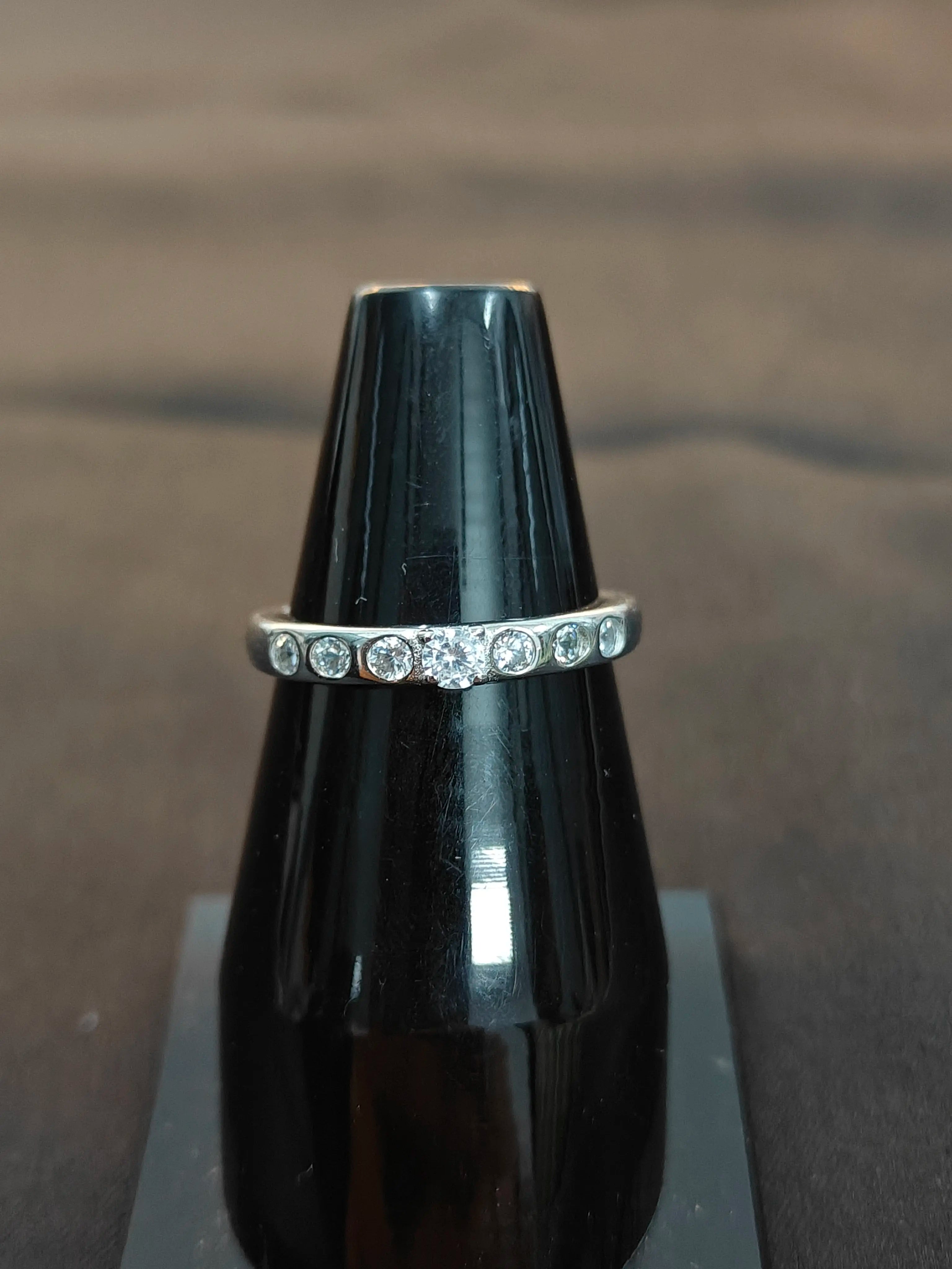 Silver ring with small stones on a black stand against a brown background