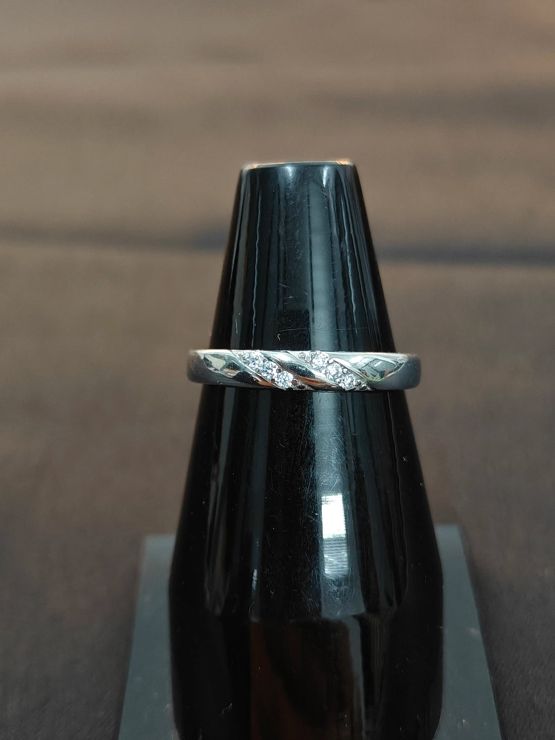 Silver ring with intricate design on a black stand against a brown background