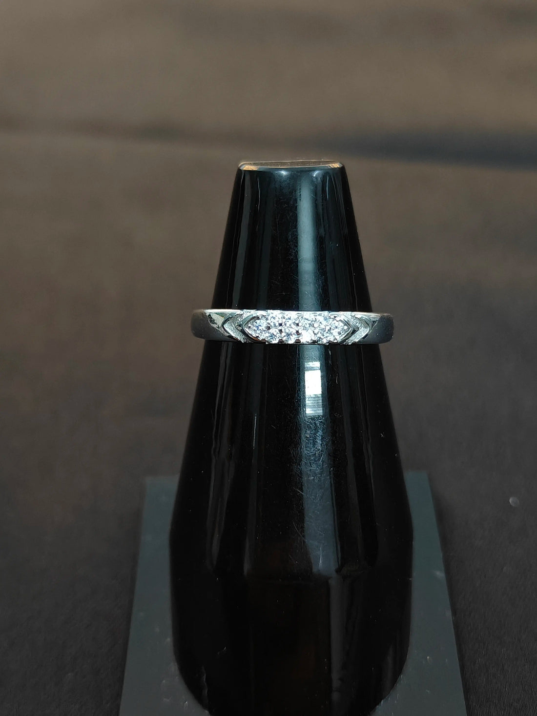 Silver ring with diamonds on a black stand against a dark background