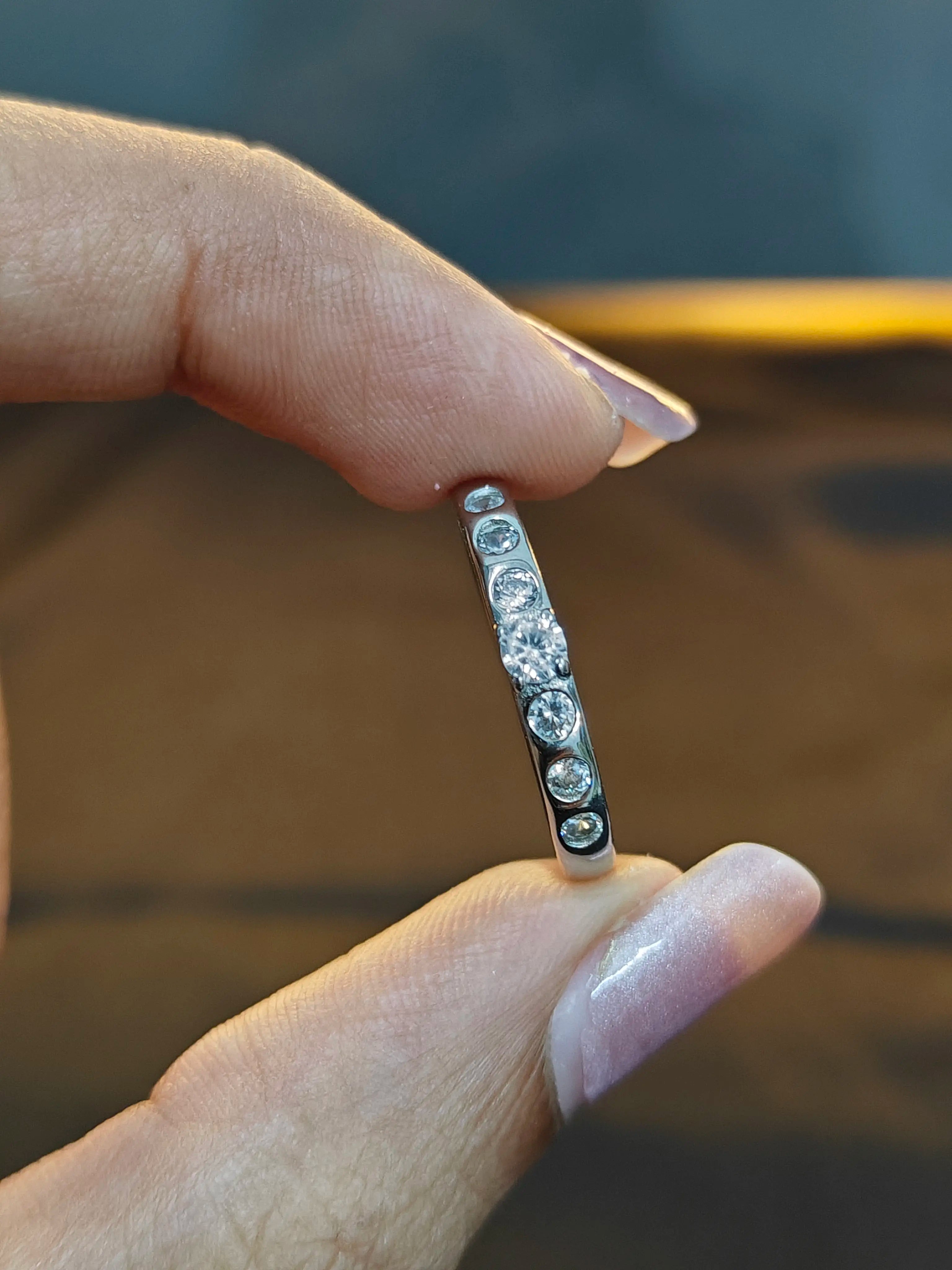 Silver ring with embedded stones held between fingers against a blurred background
