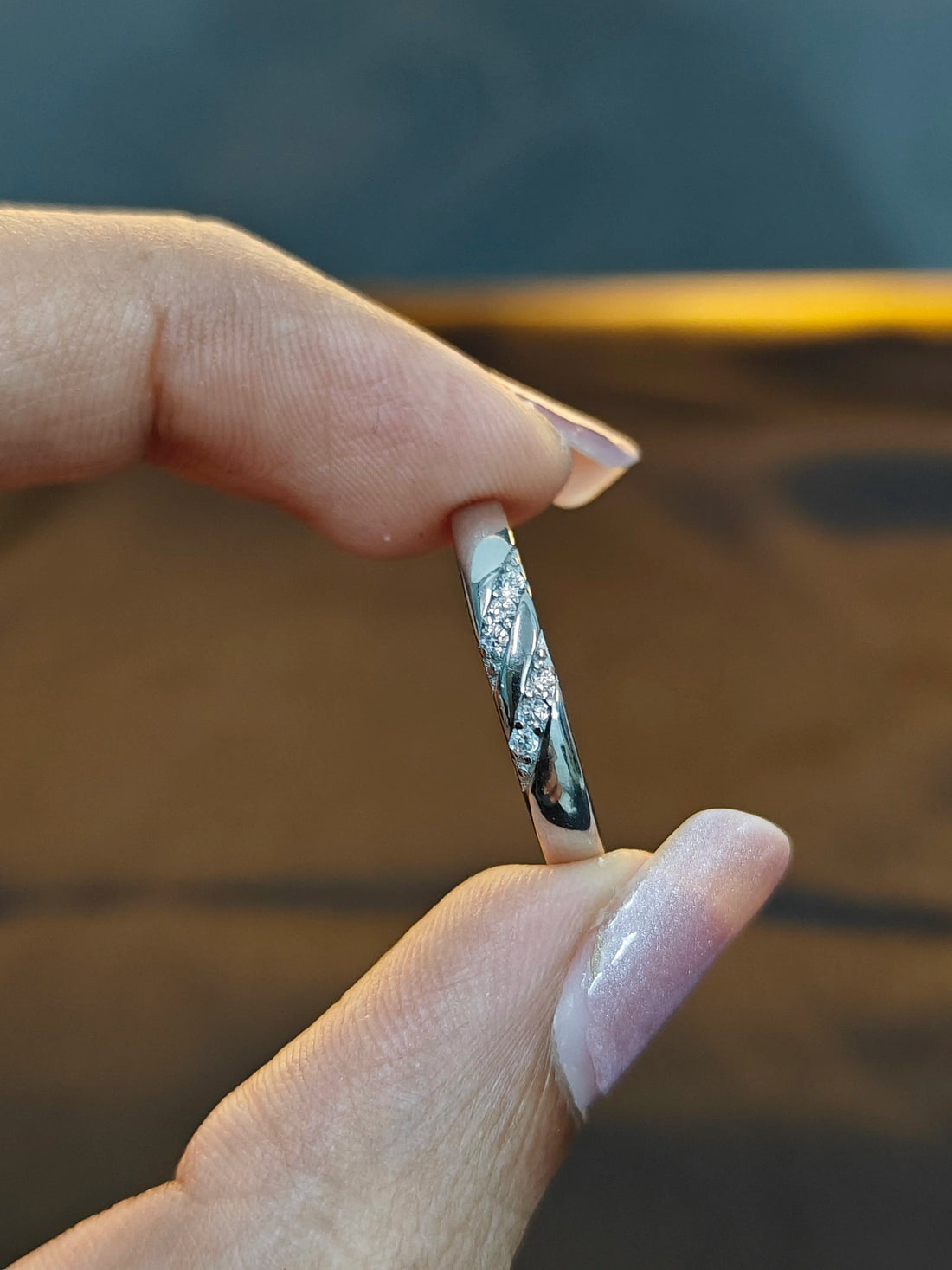 Hand holding a silver ring with a mountain design against a blurred background