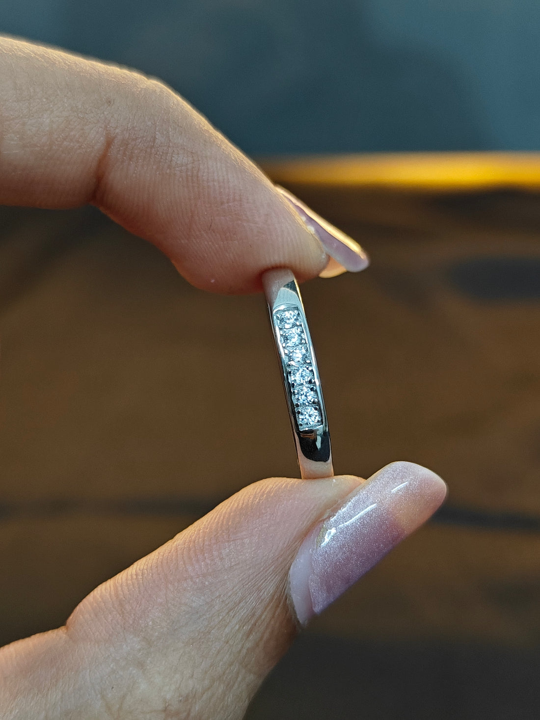 Close-up of a hand holding a diamond ring with a blurred background