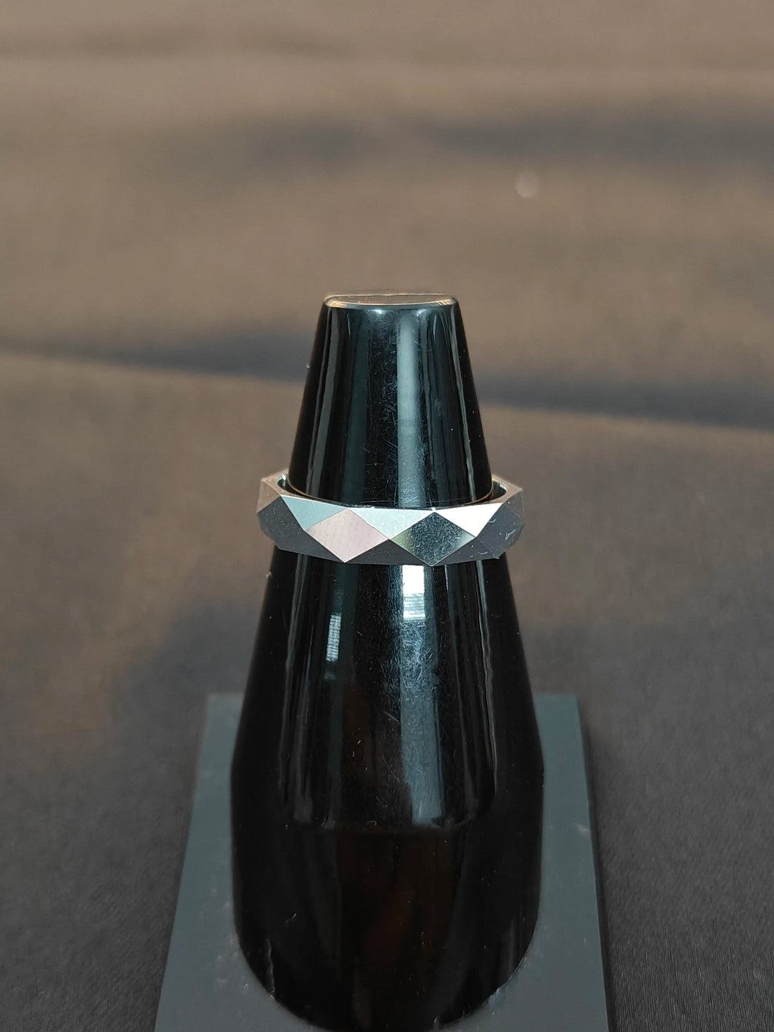Silver ring with geometric design on a black vase against a dark background