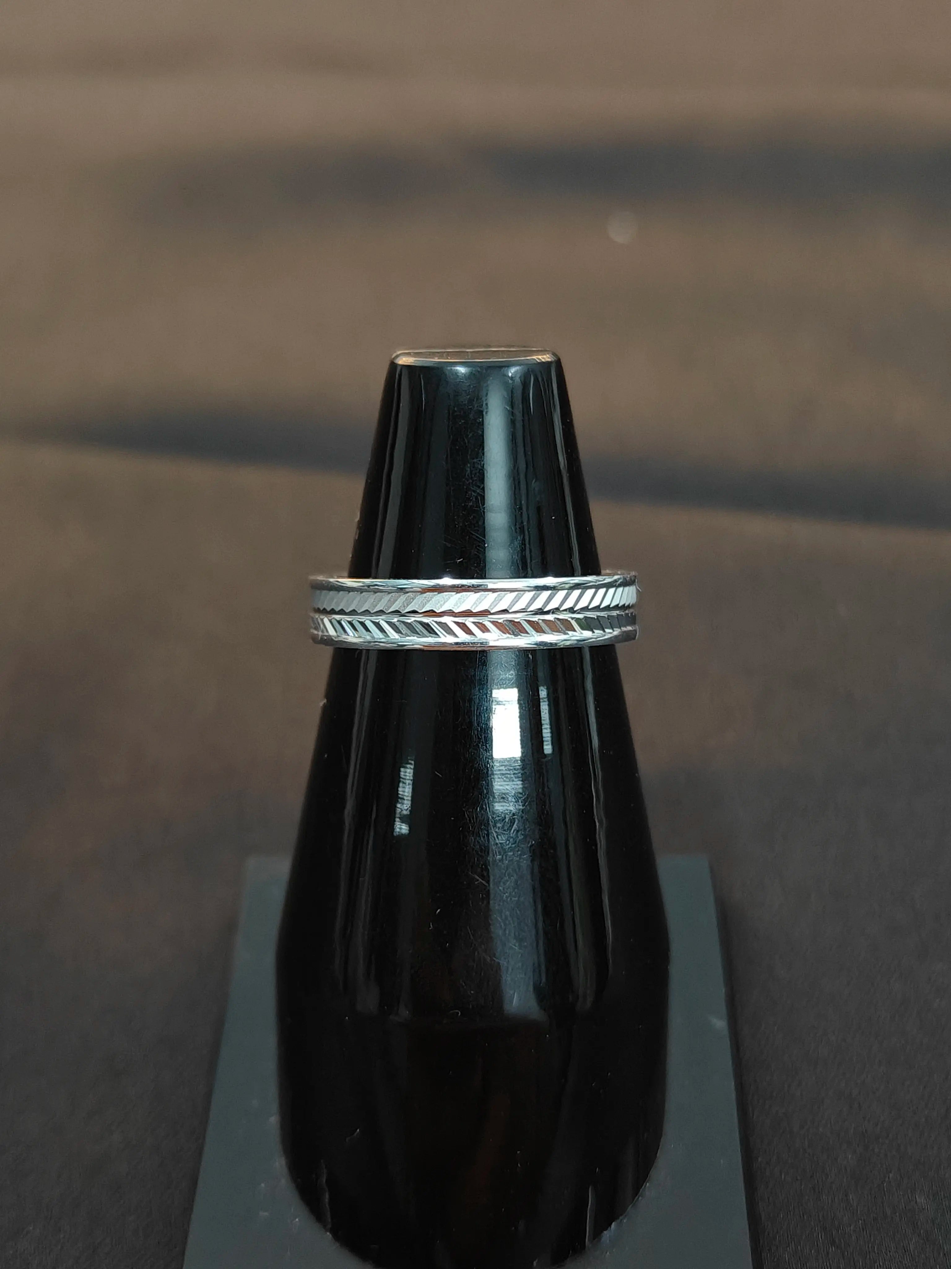 Silver ring with a textured band on a black stand against a dark background