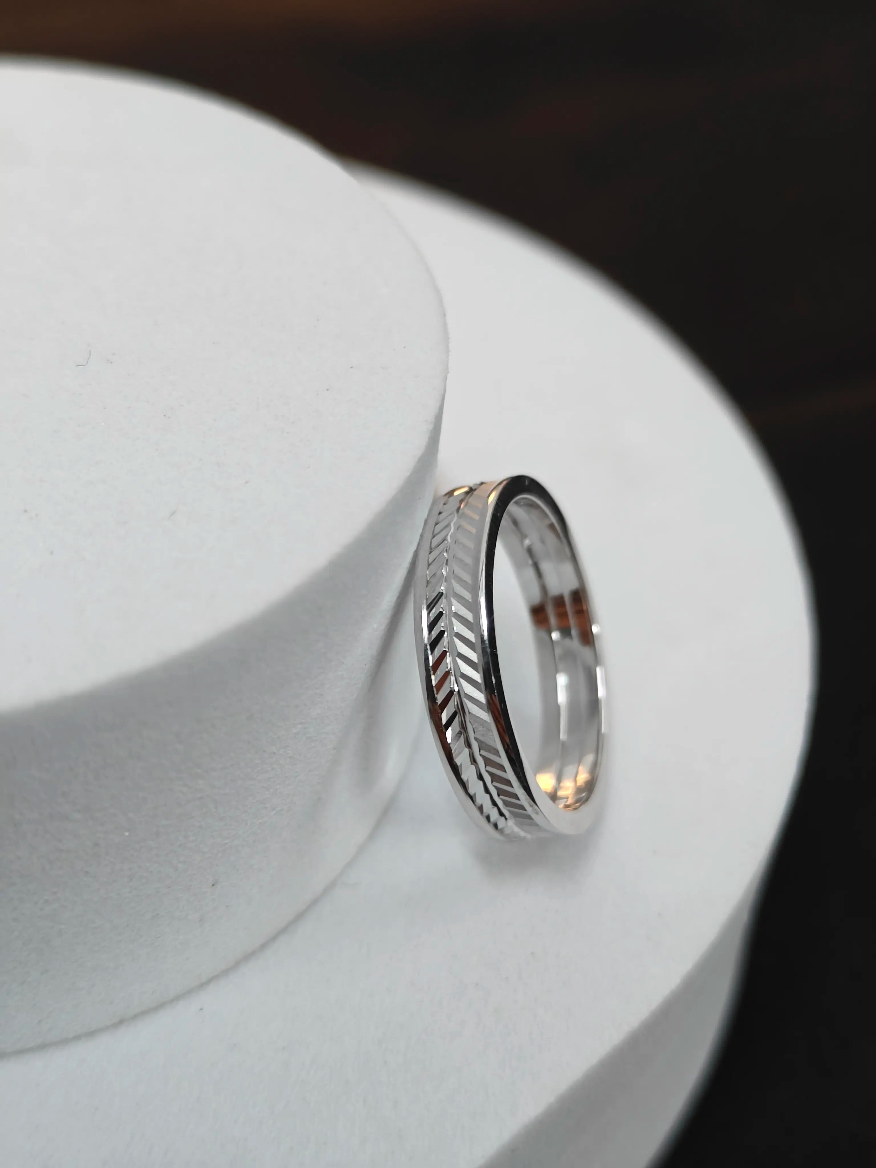 Silver ring with a textured design on a white stand