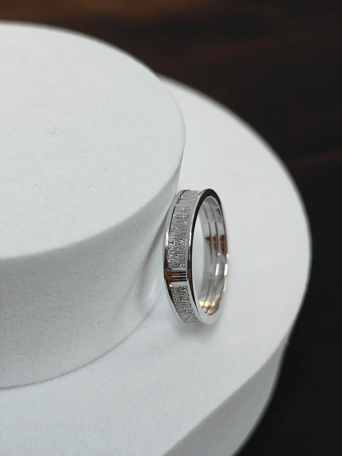 Silver ring with textured band on a white stand