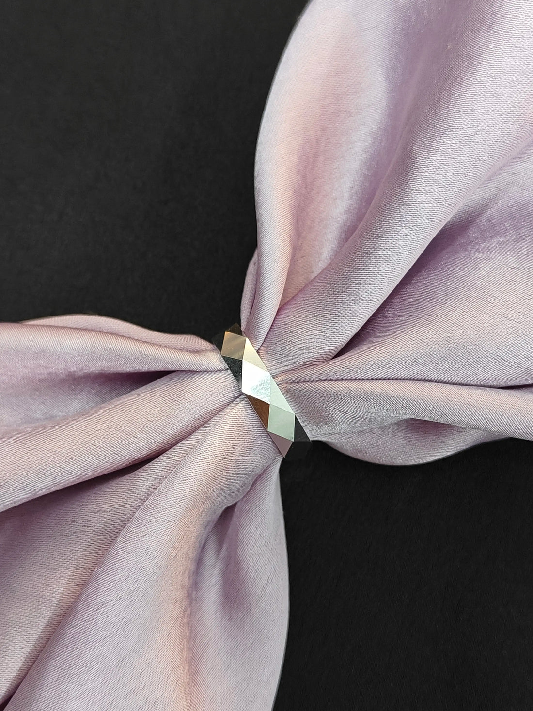 Close-up of a knotted lavender fabric with a metallic ring on a black background