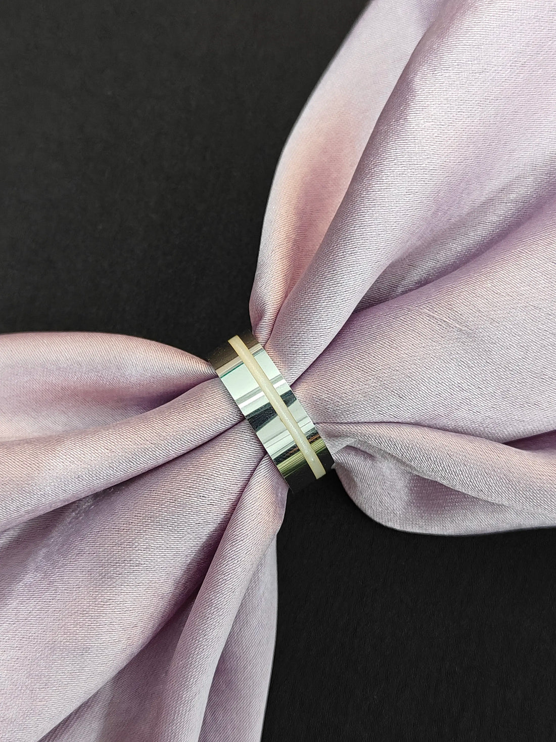 Gold ring on a pink fabric bow against a black background