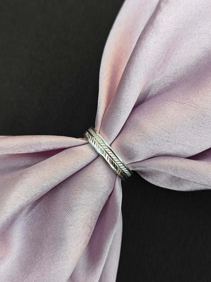 Silver ring with a feather design on a pink fabric background
