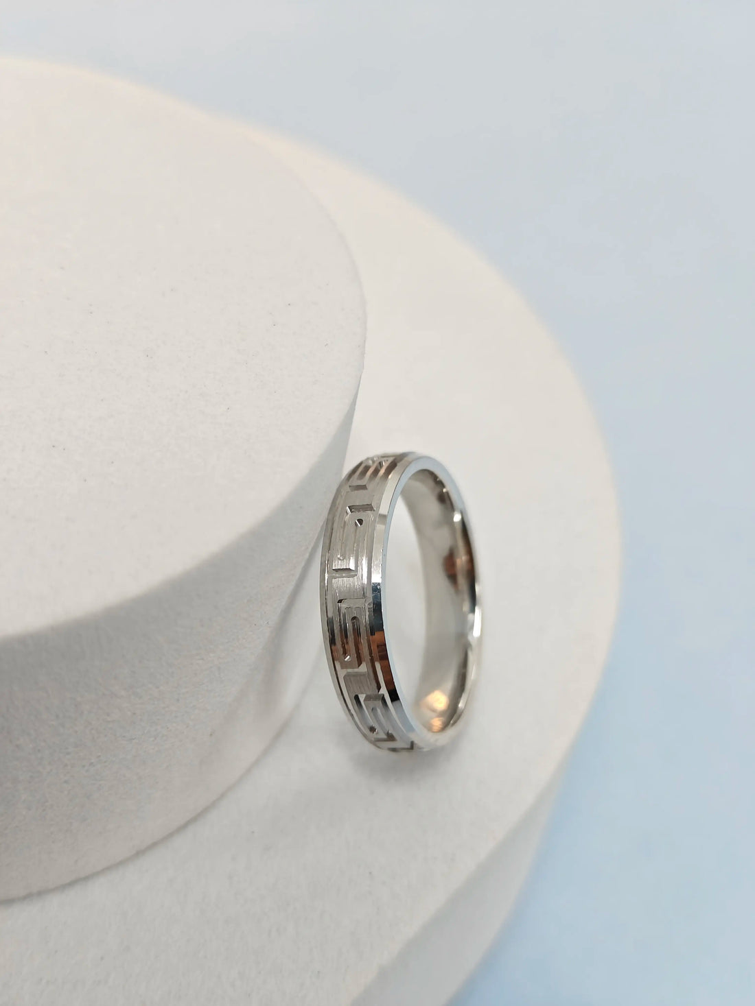 Silver ring with a geometric design on a white stand against a light blue background
