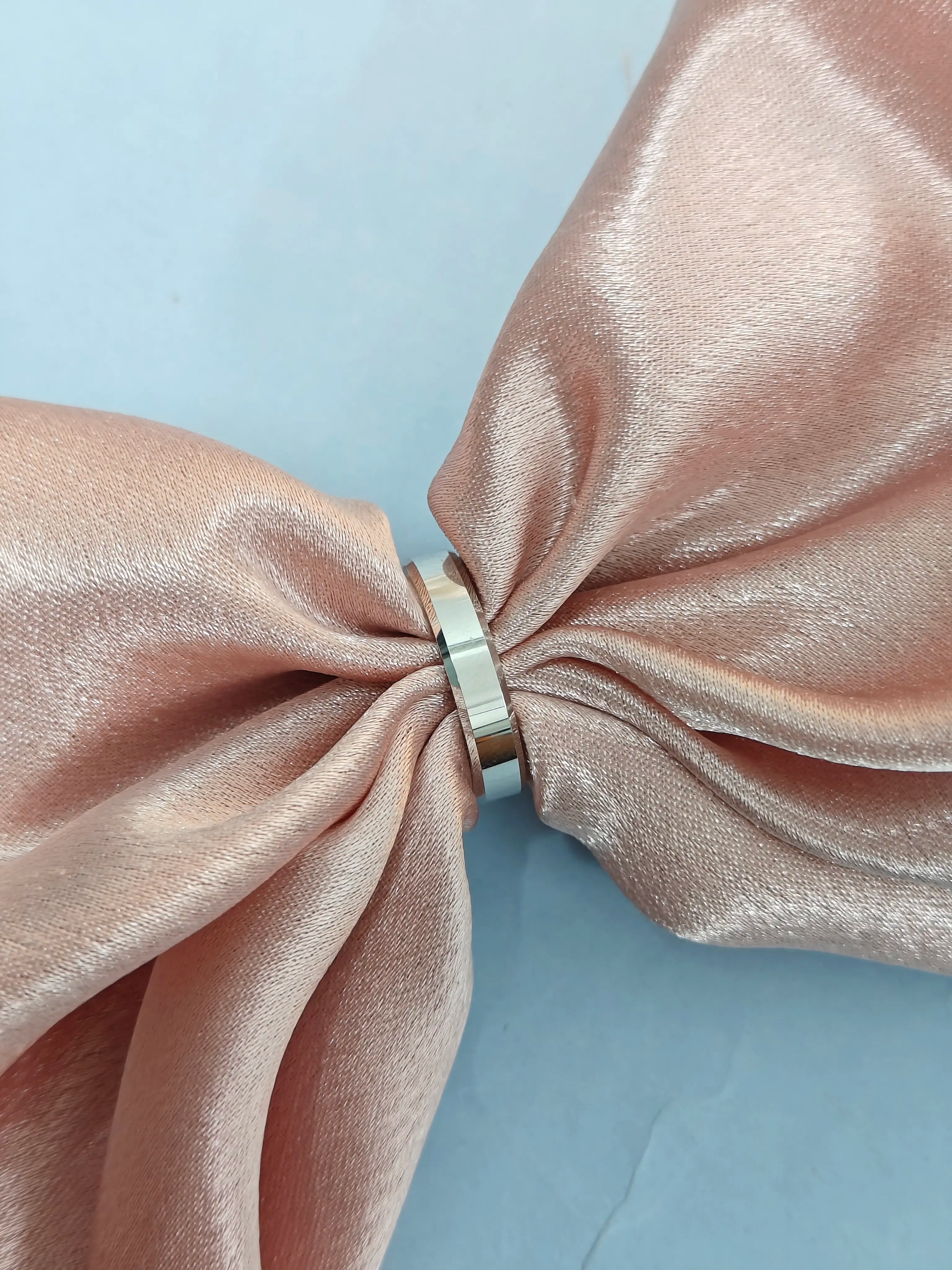 Pink satin bow with a silver ring on a light blue background