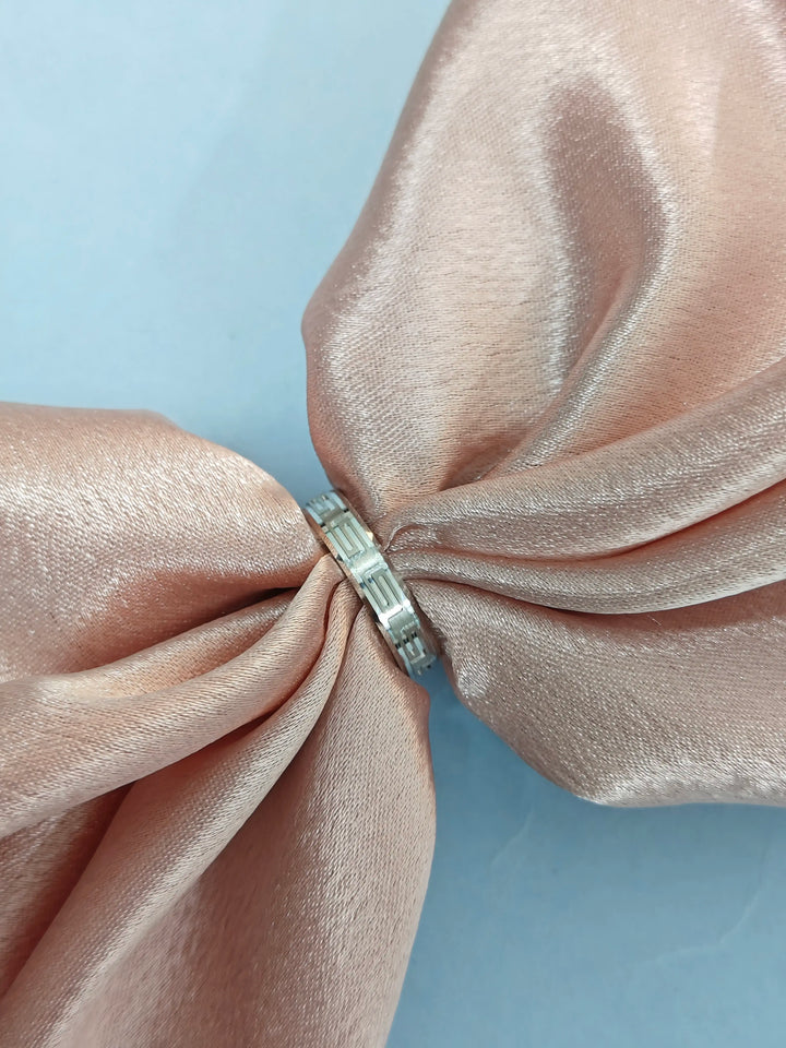 Silver ring on a pink satin bow with a light blue background