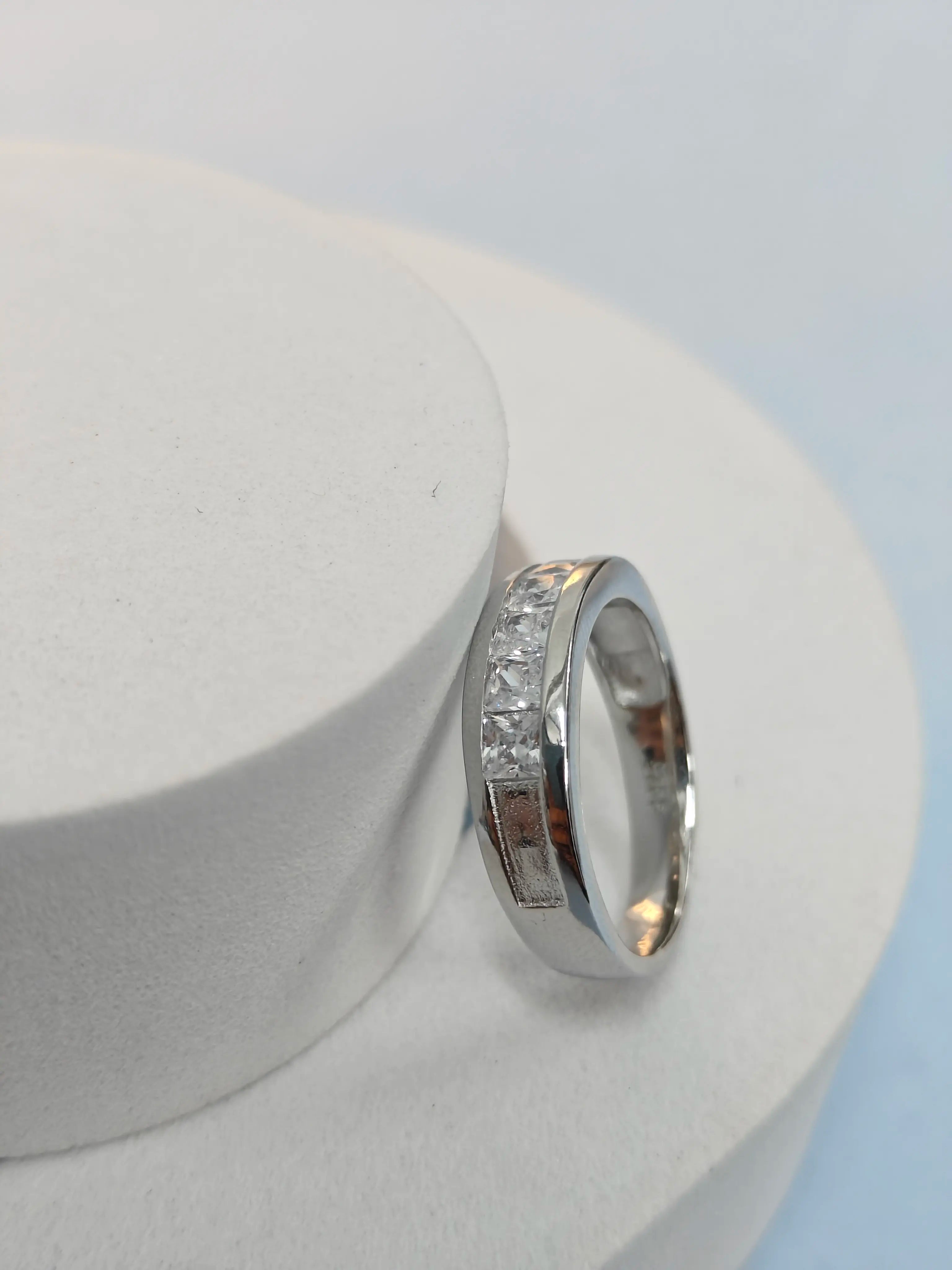 Silver ring with embedded stones on a white stand against a light blue background