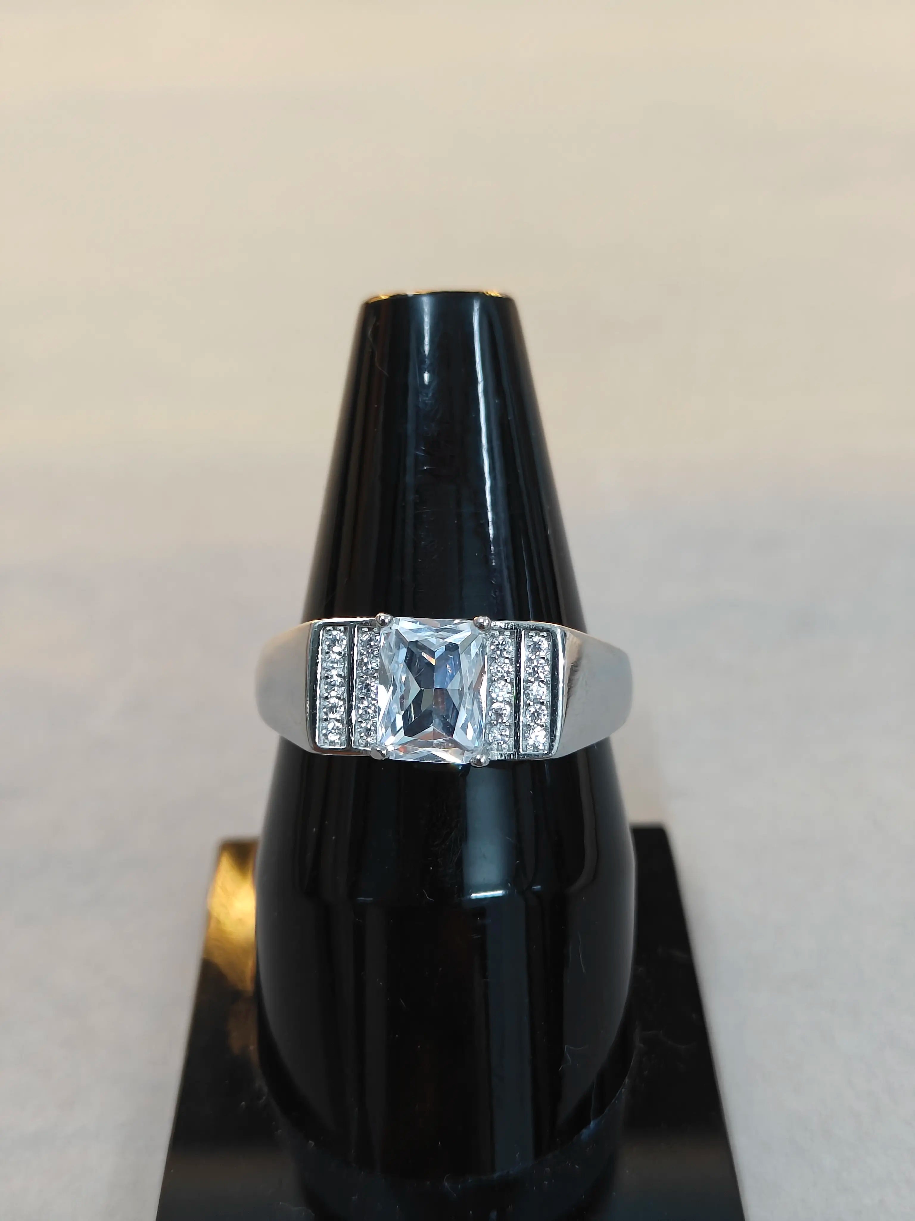 Silver ring with a large central diamond and smaller diamonds on the band, displayed on a black stand.