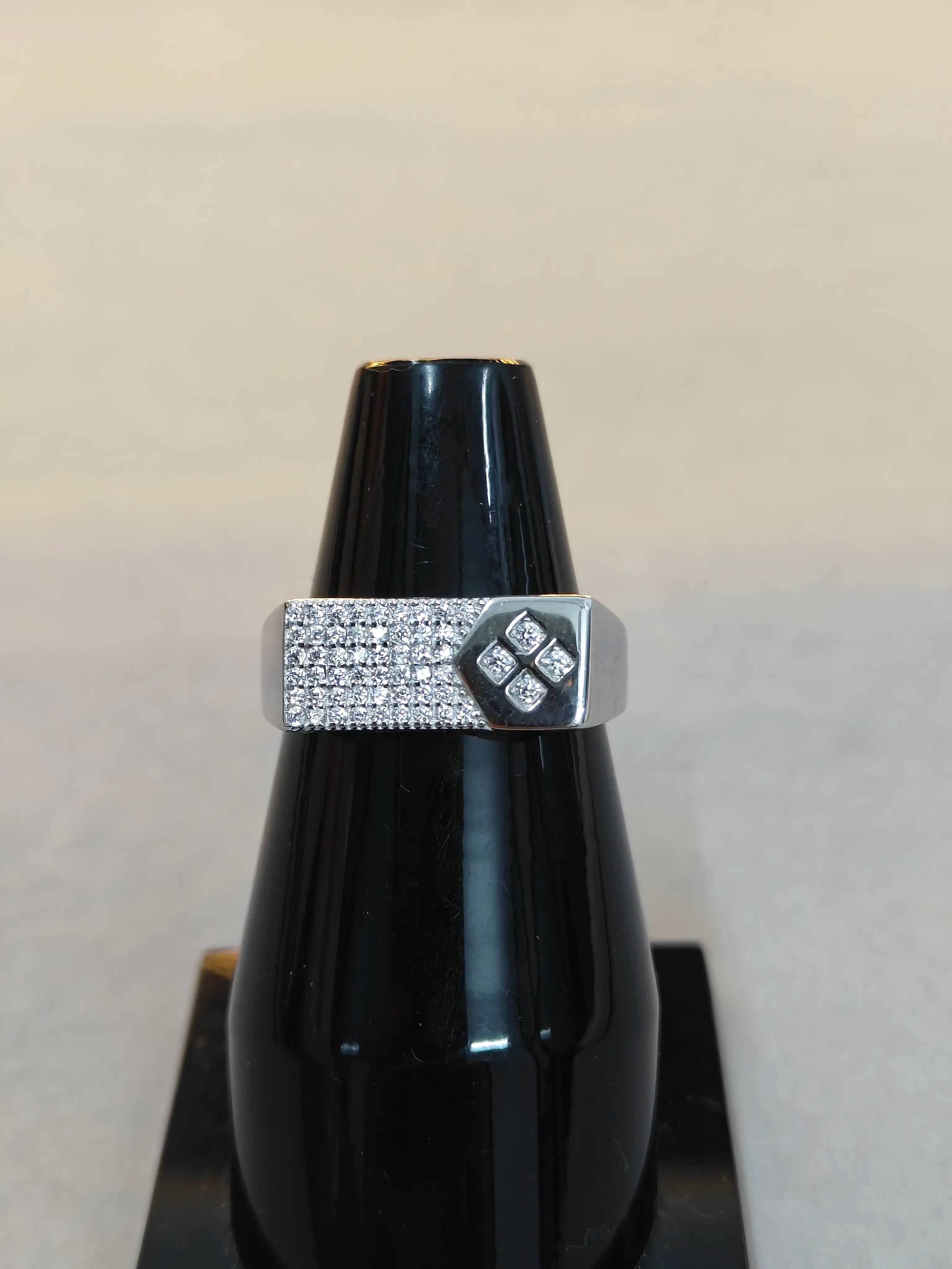 Silver ring with a diamond design on a black stand against a beige background