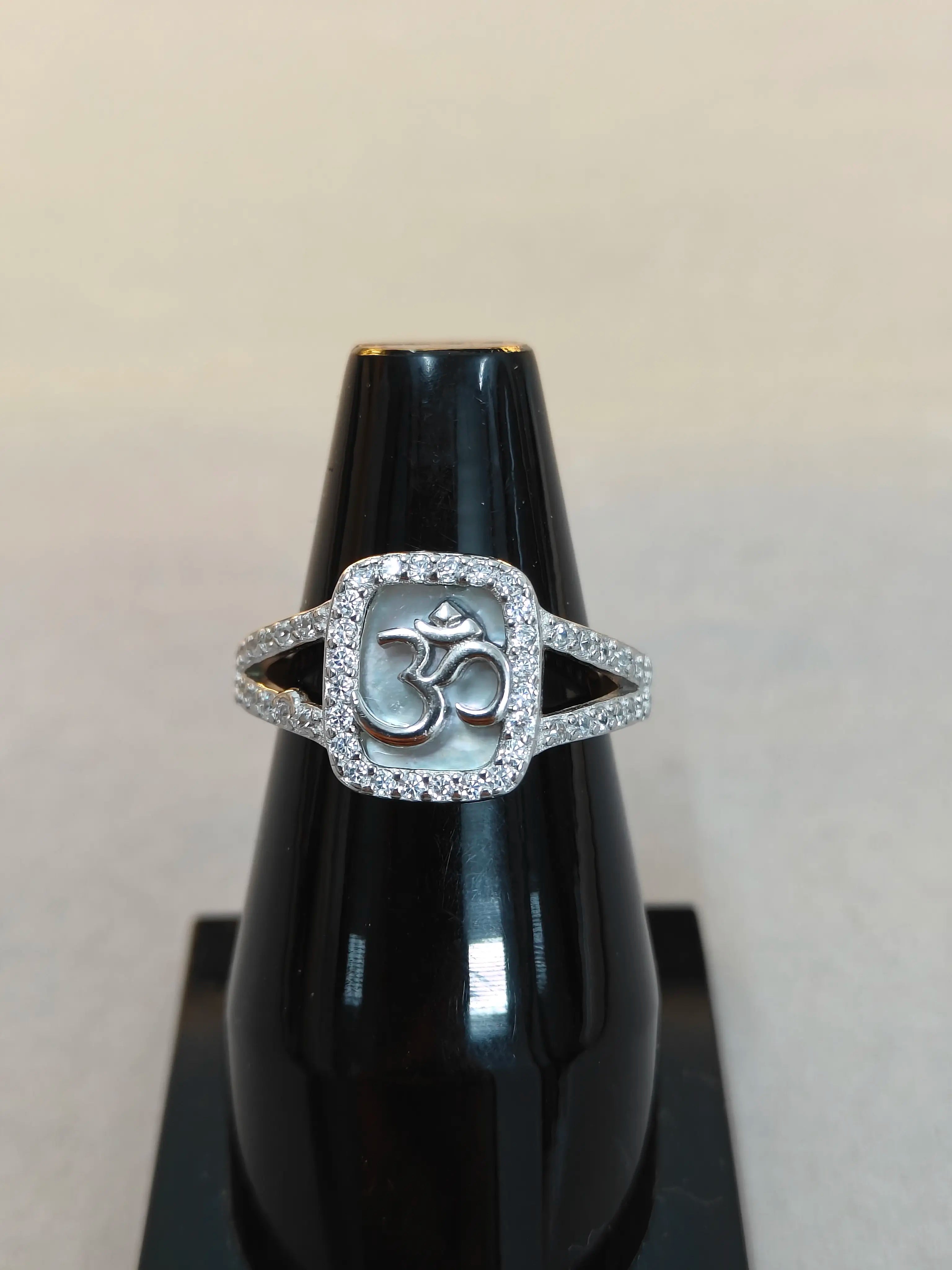 Silver ring with a central symbol on a black stand against a light gray background