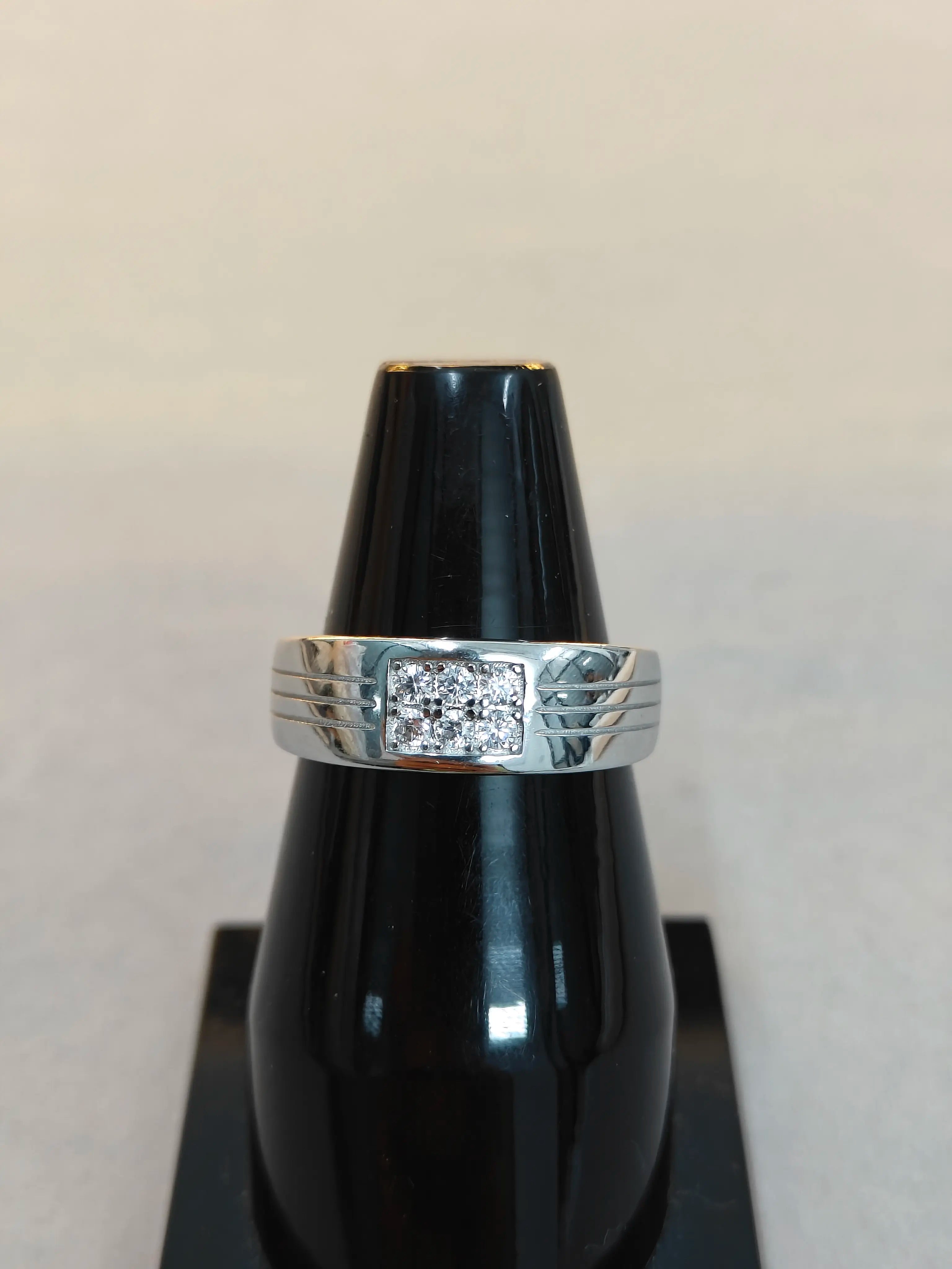 Silver ring with a diamond on a black stand against a beige background
