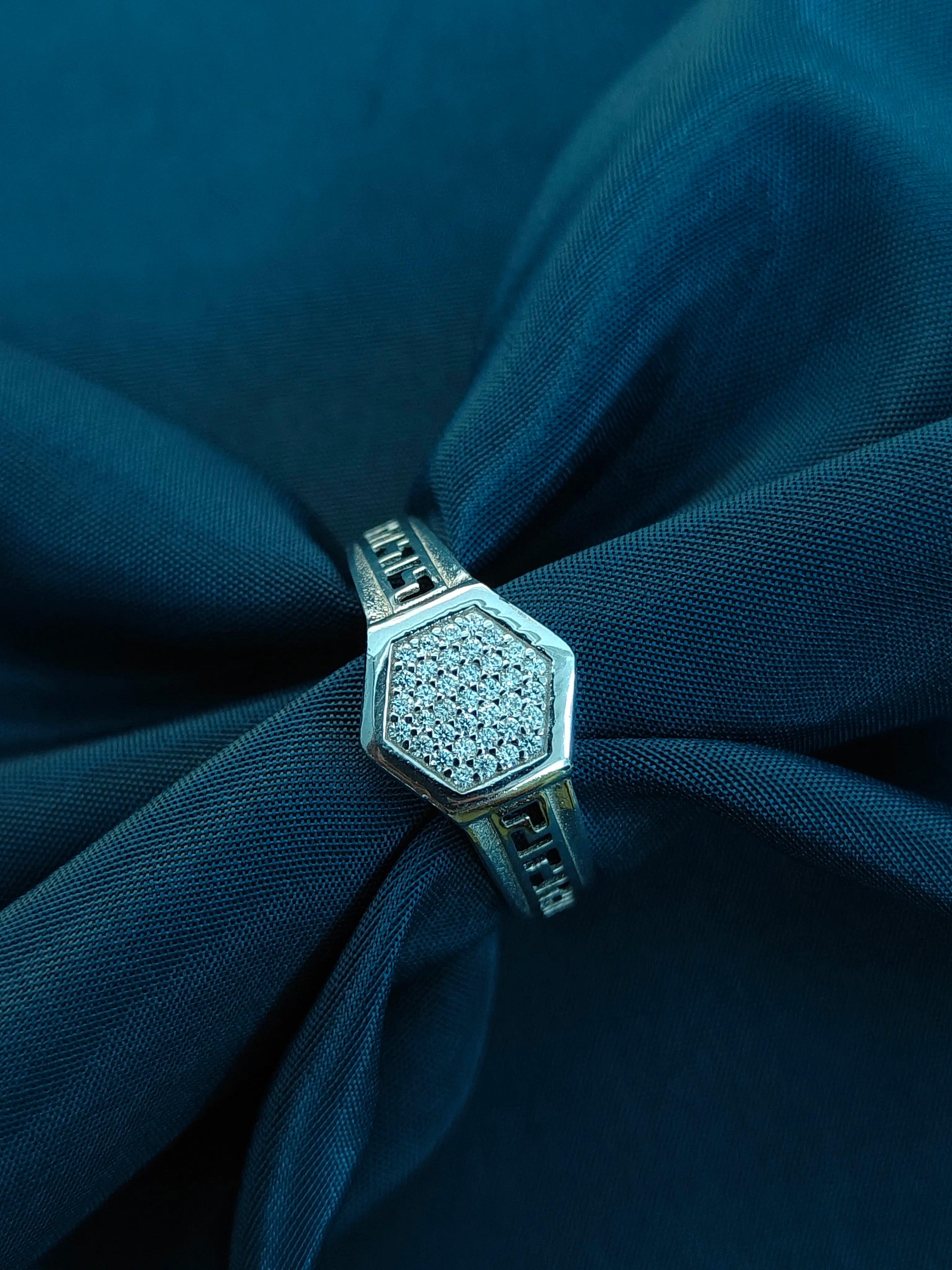 Silver ring with a diamond hexagonal design on a dark blue fabric background