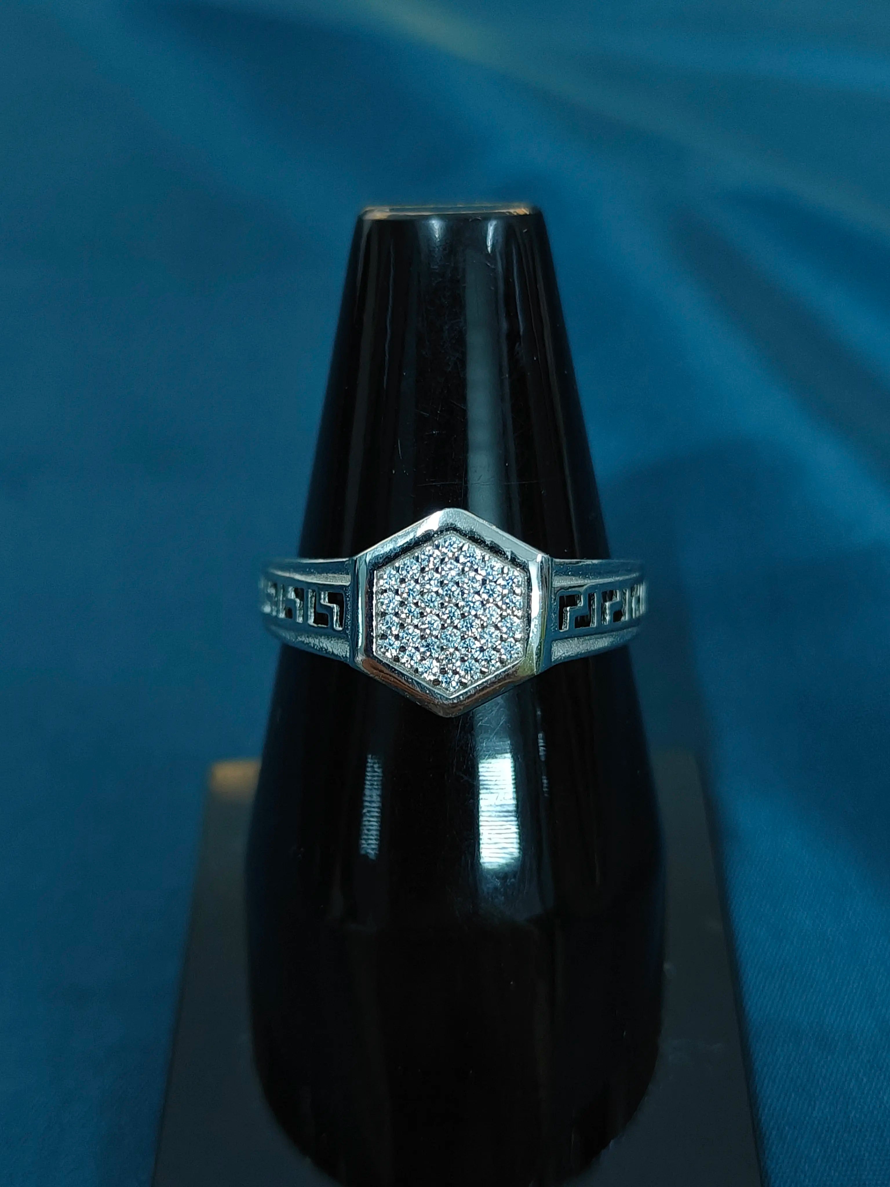 Ring with diamond-studded hexagonal design on a black stand against a blue background