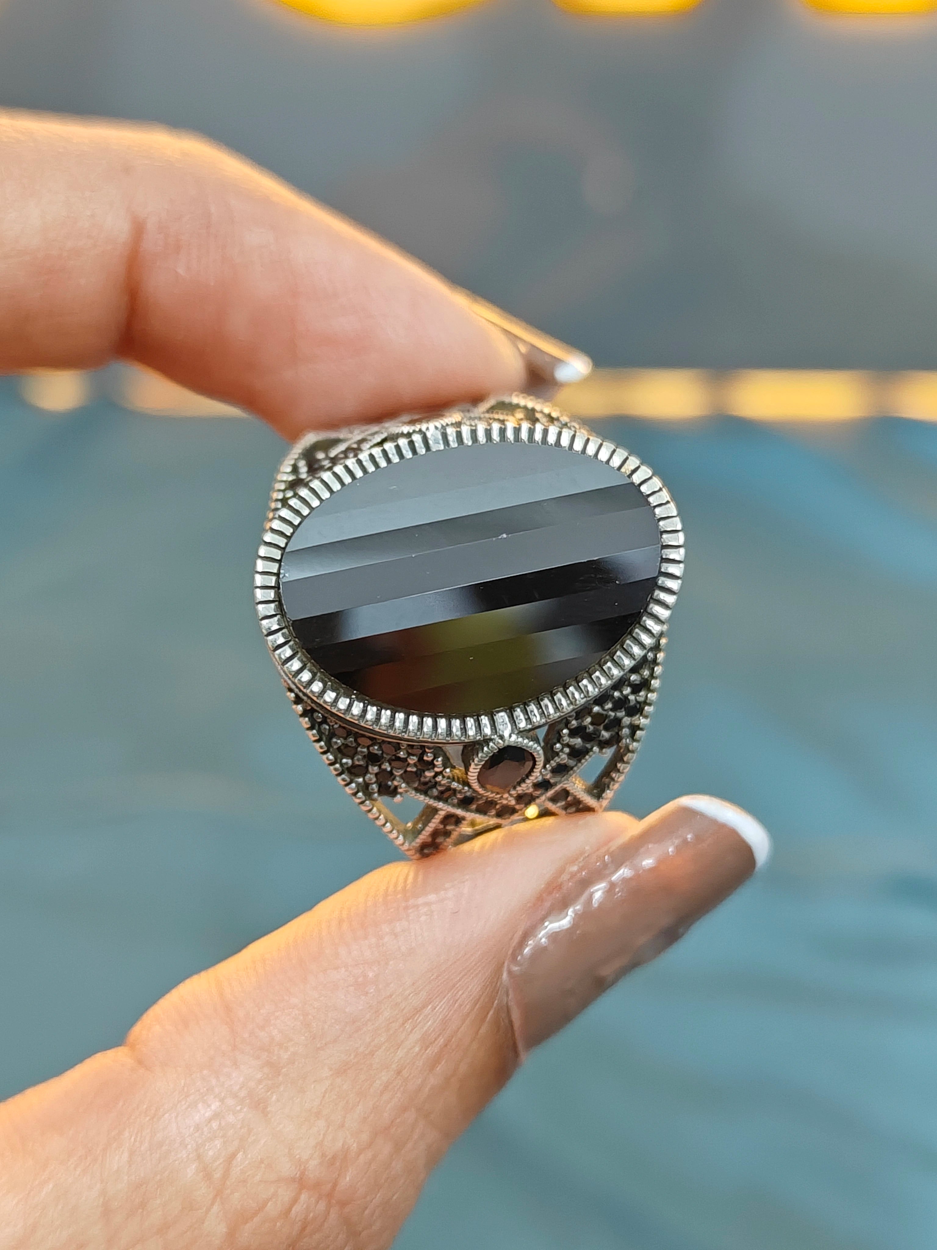 Silver ring with a black stone held on a blurred background