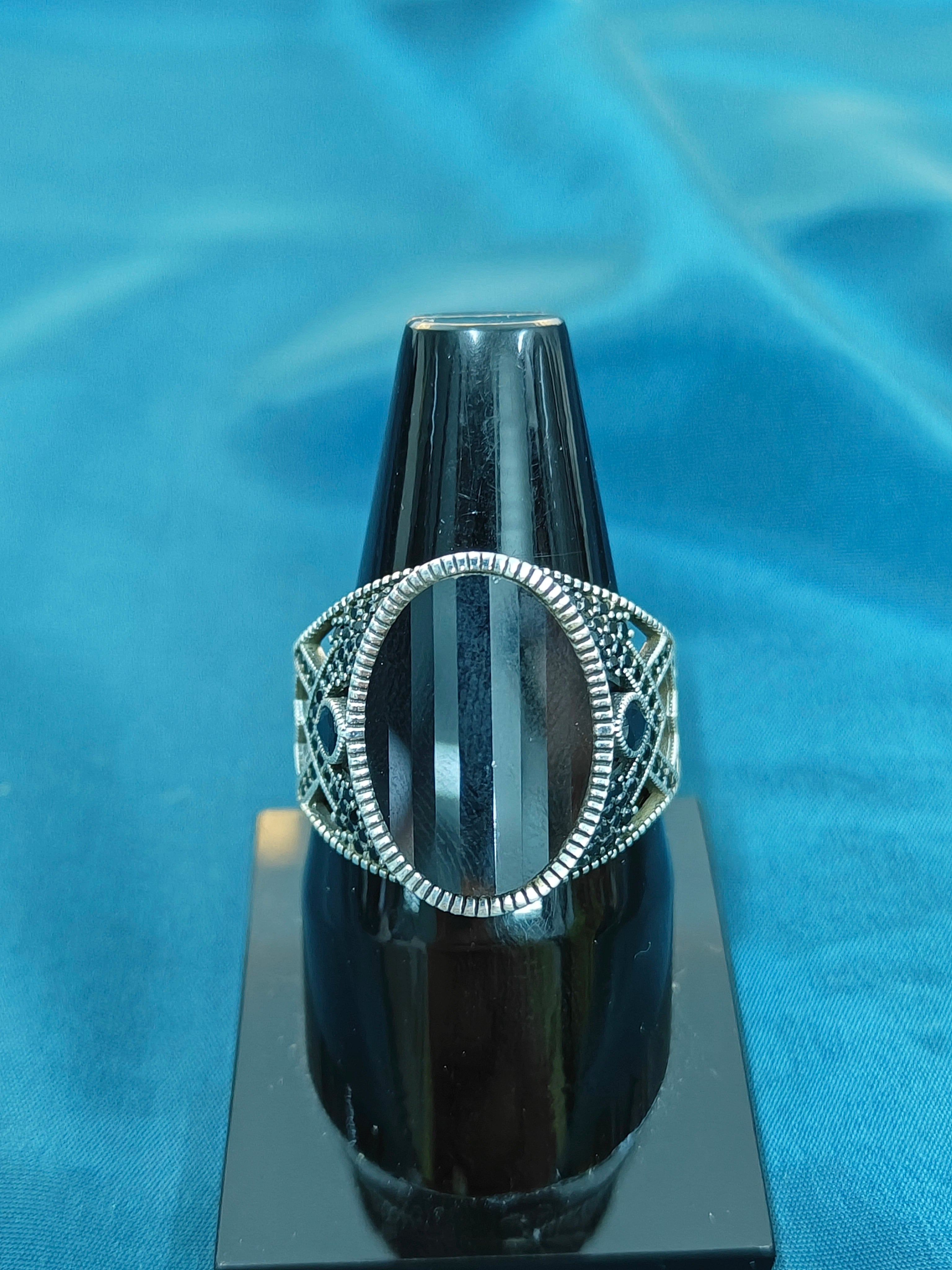 Silver ring with intricate design on a black stand against a blue fabric background