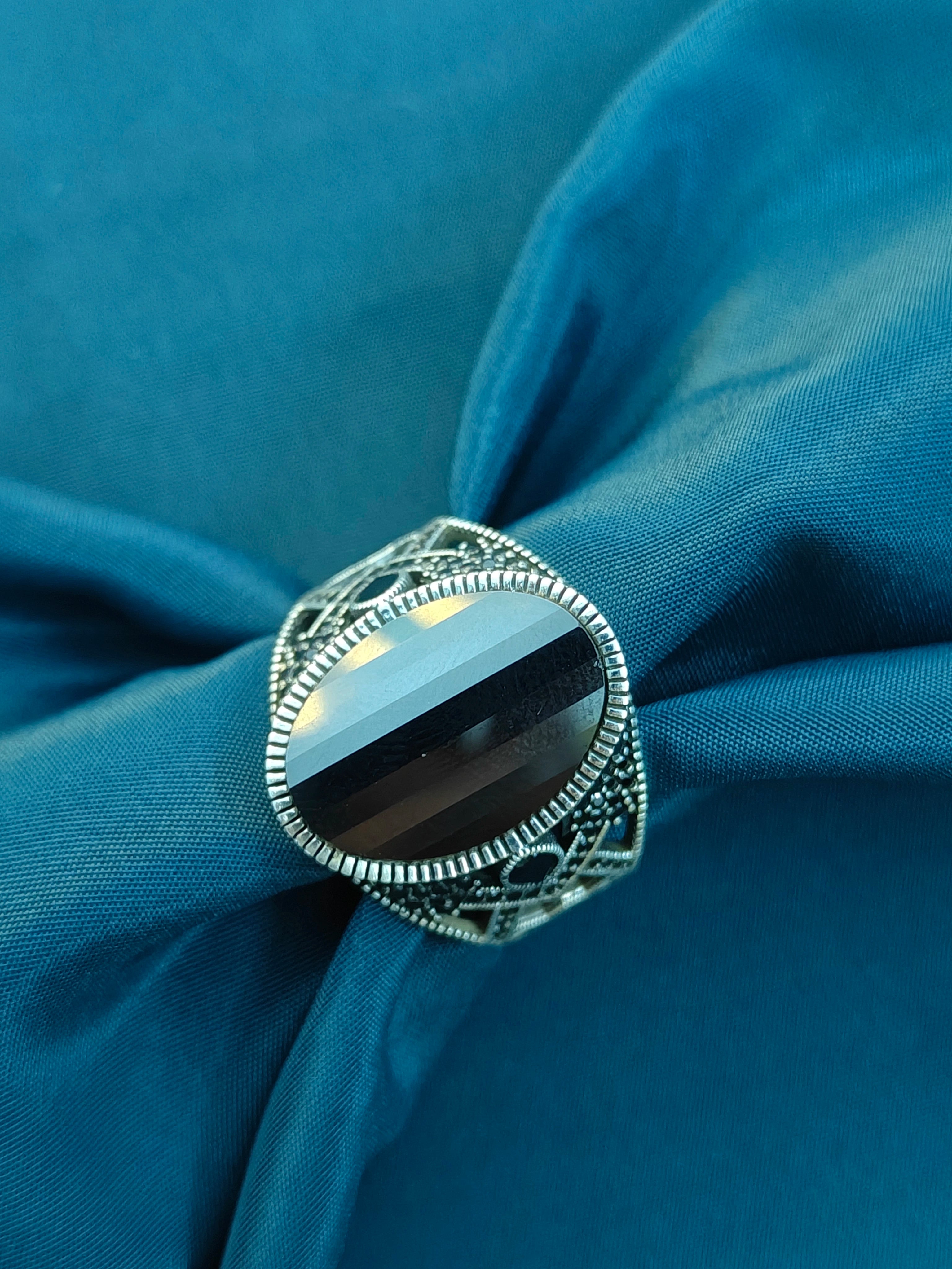 Silver ring with black stone on a blue fabric background