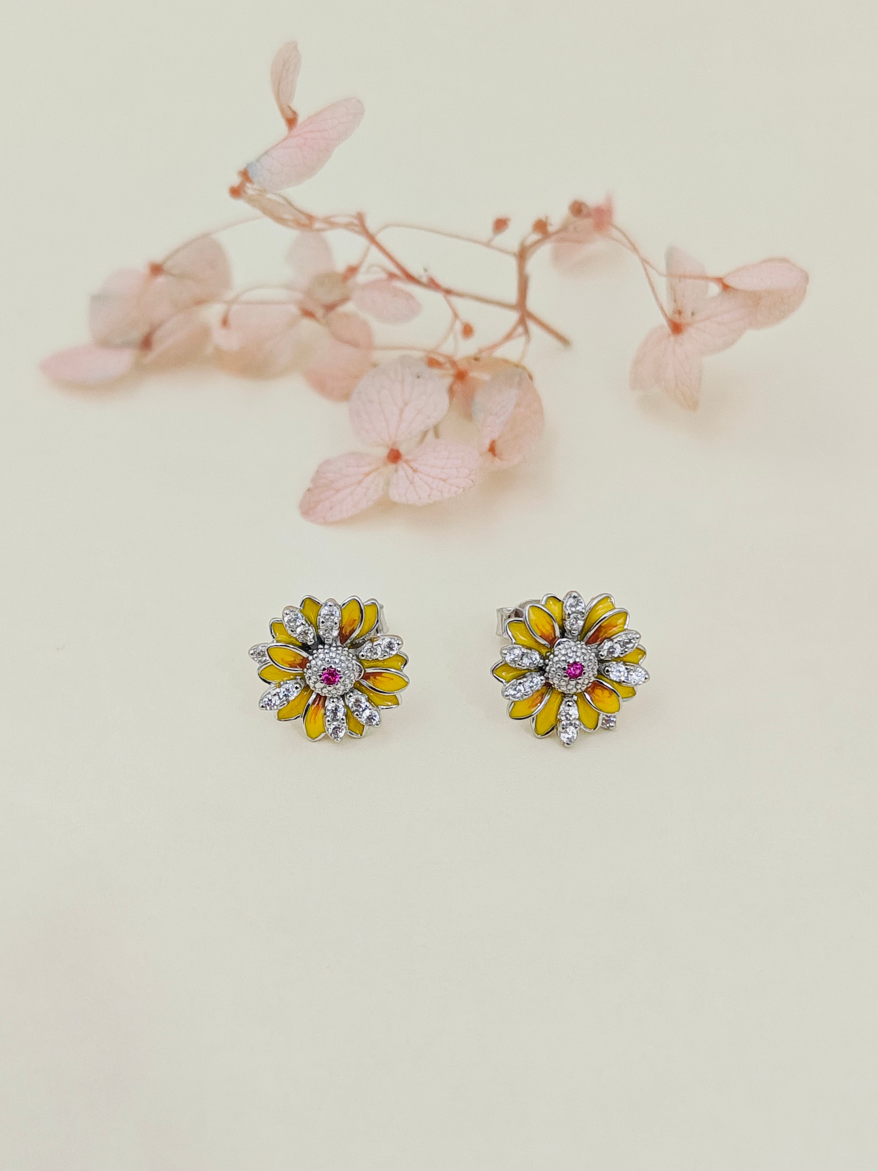 Pair of floral earrings with yellow centers and pink stones on a light background.