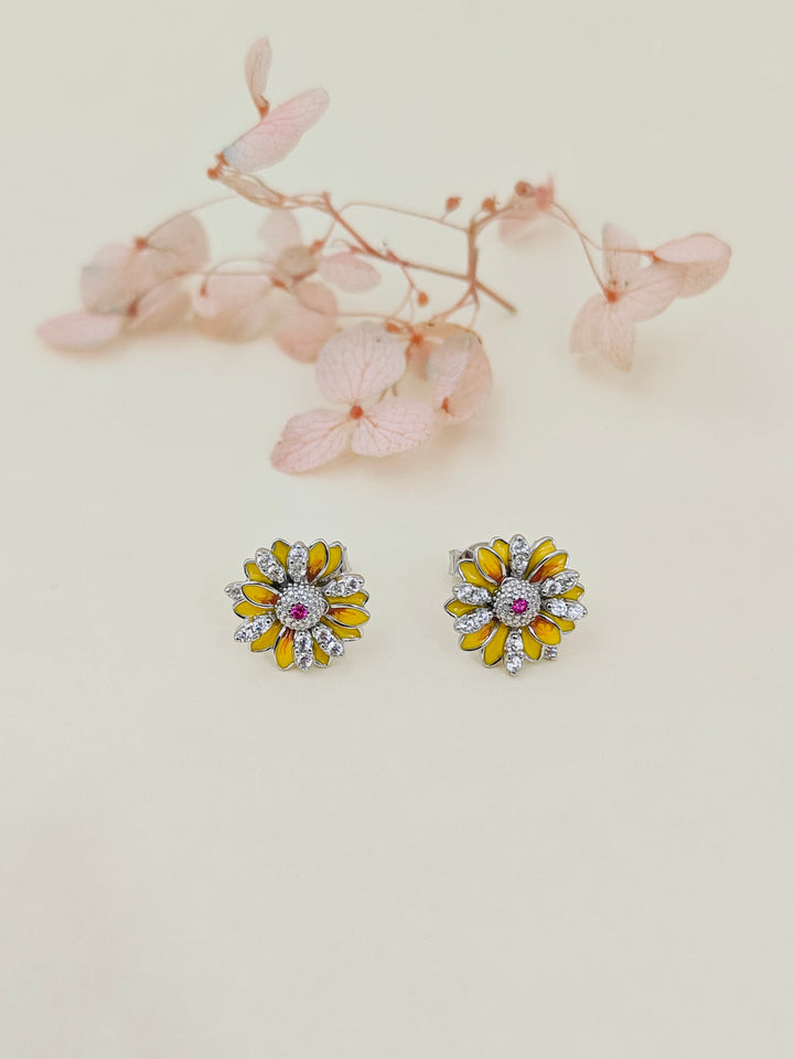 Pair of floral earrings with yellow centers and pink stones on a light background.
