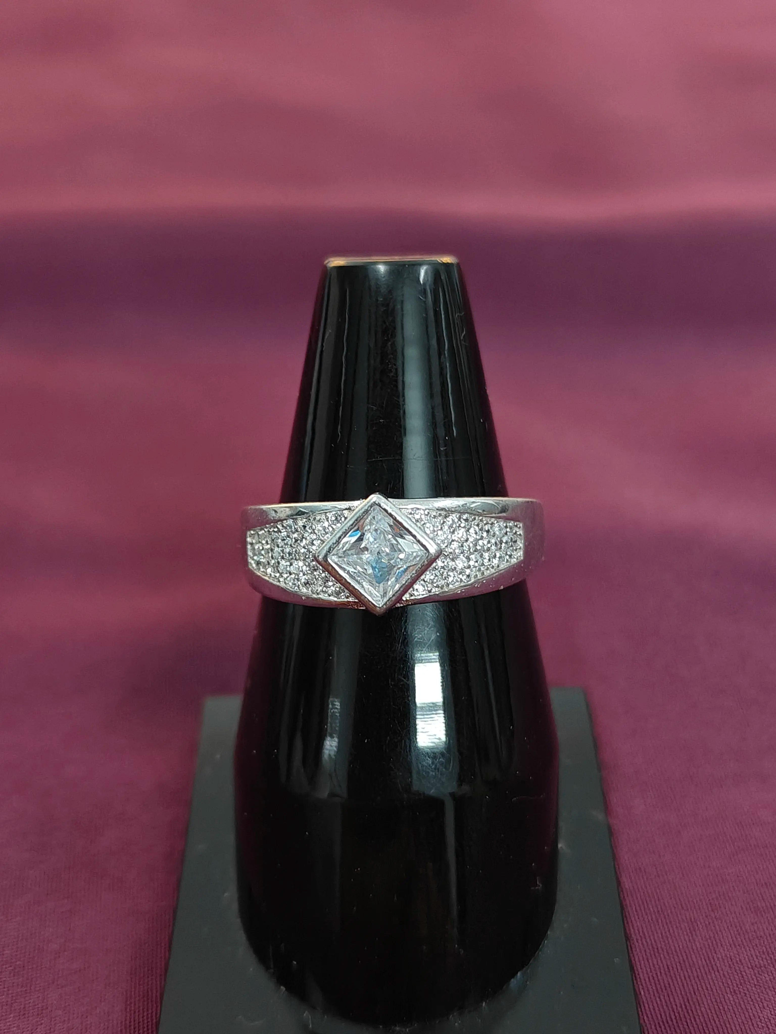 Silver ring with a central gemstone on a black vase against a purple fabric background