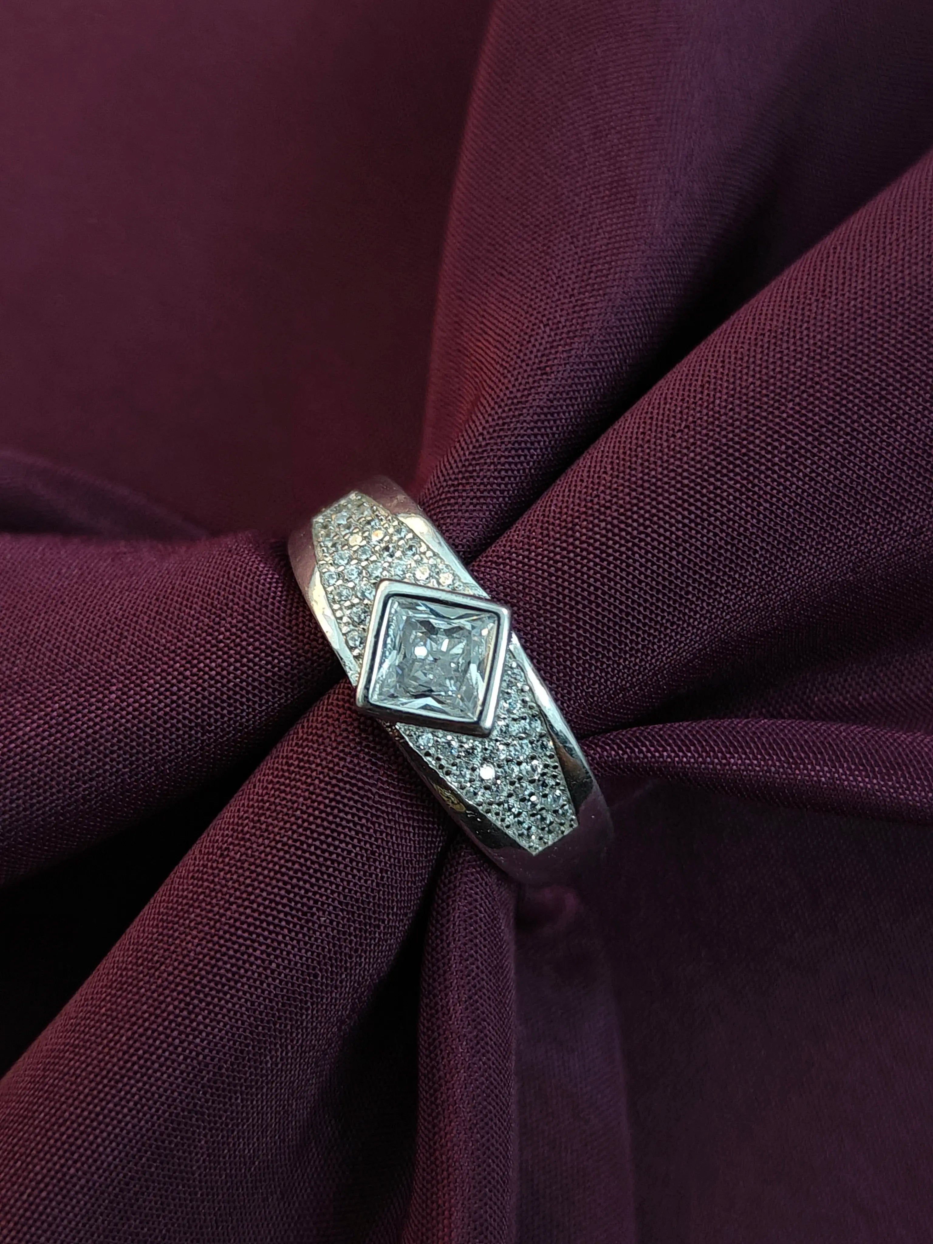 Silver ring with a diamond on a purple fabric background