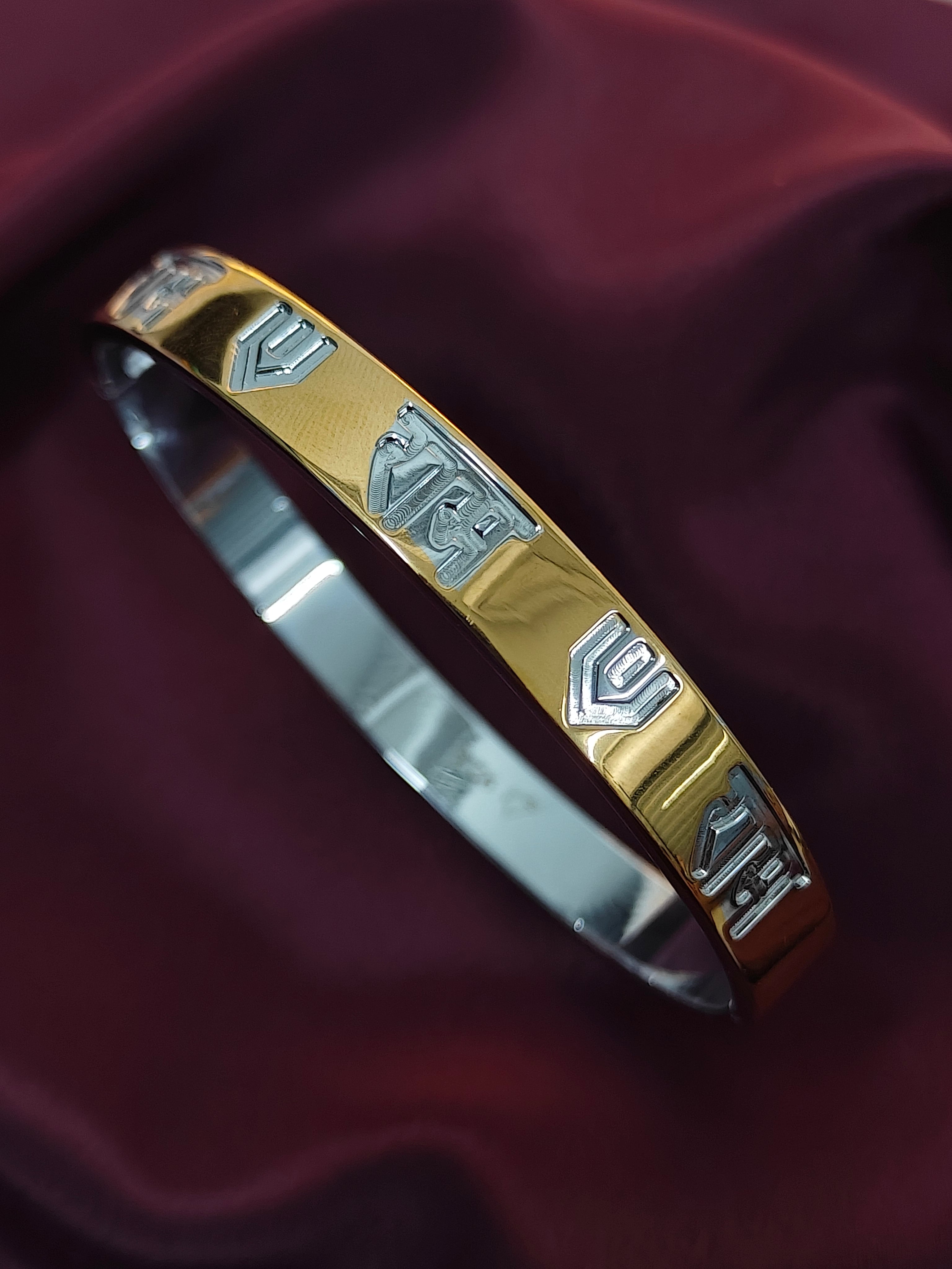 Gold and silver bracelet with engraved designs on a dark red fabric background