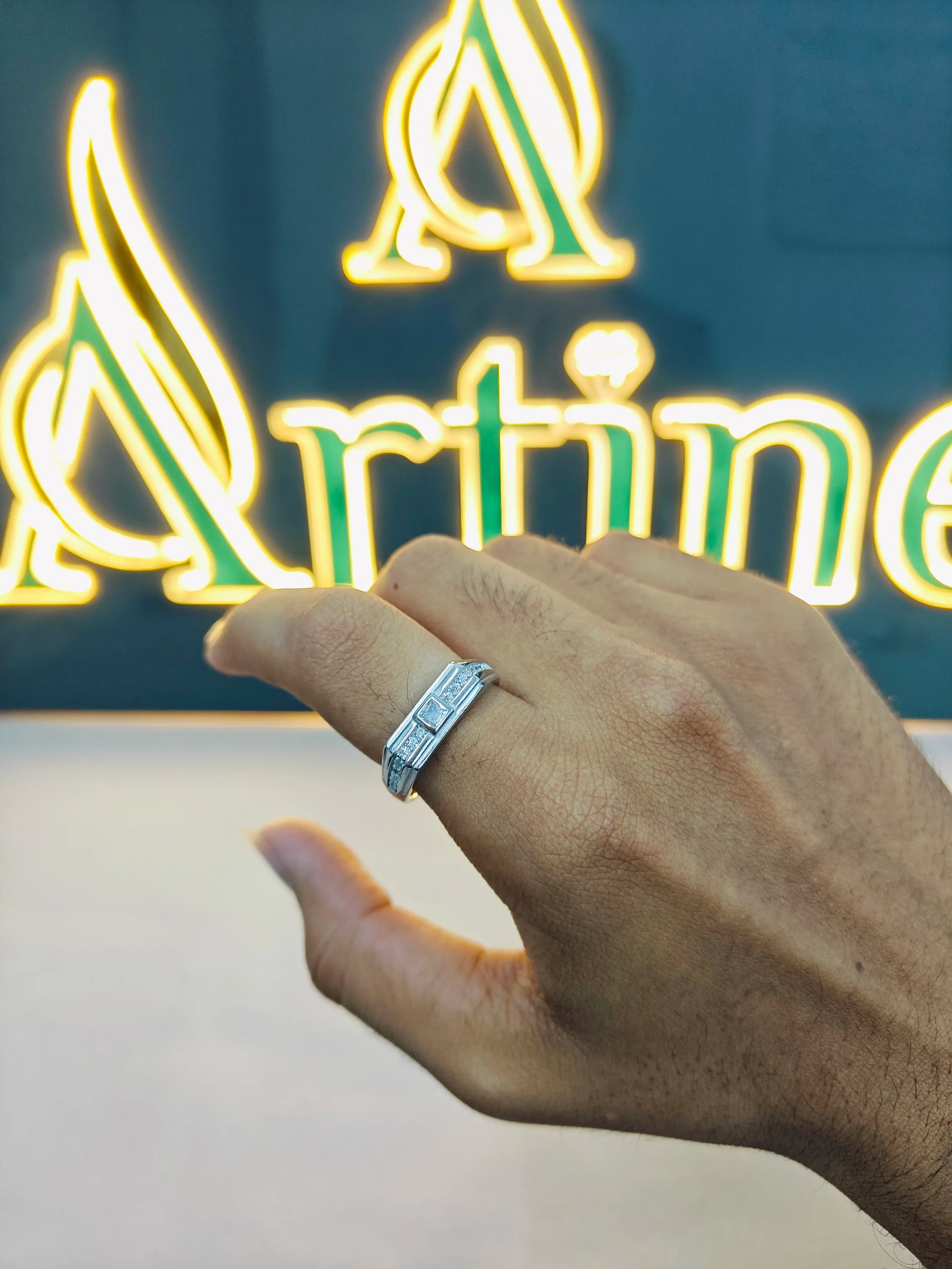 Hand wearing a silver ring with a neon sign in the background