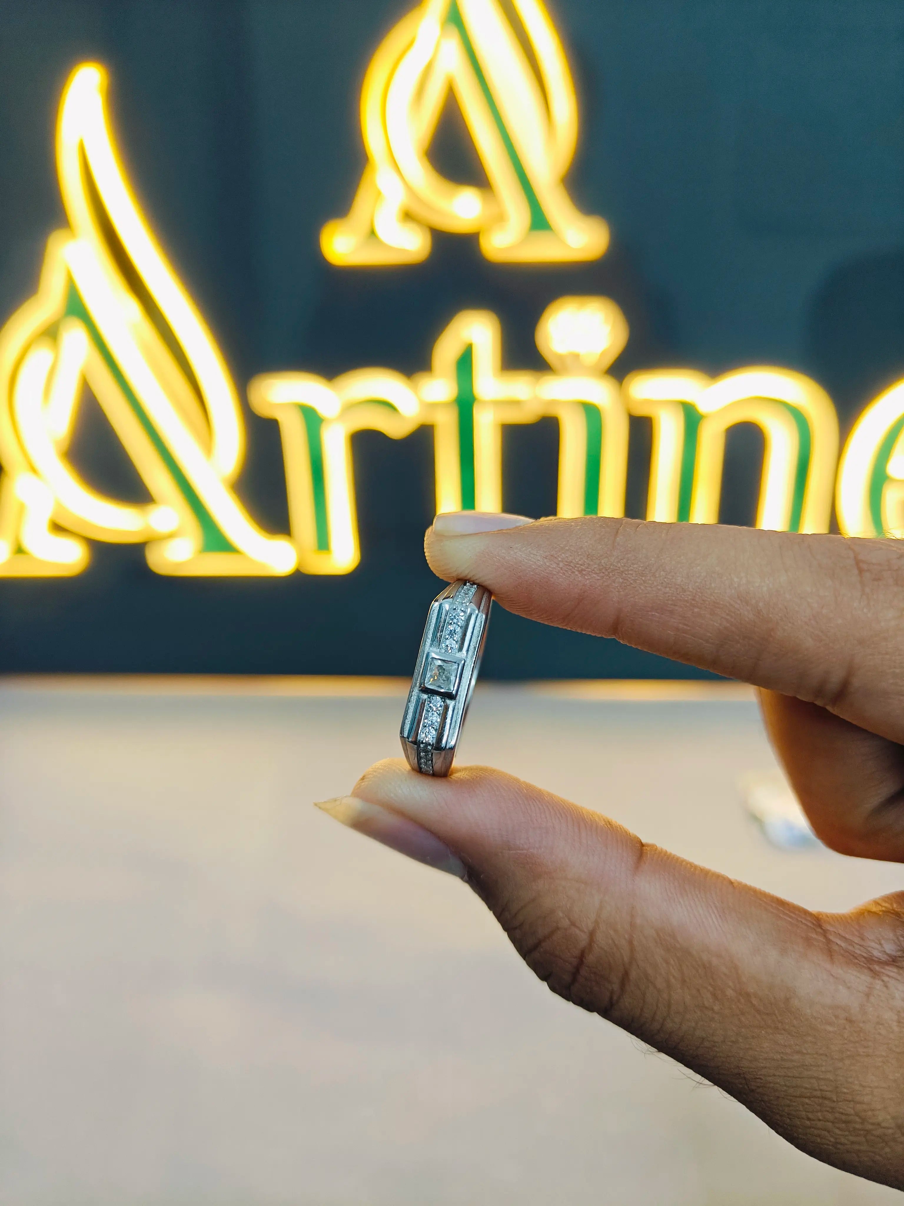 Hand holding a diamond ring in front of a neon sign with 'Artime' branding.