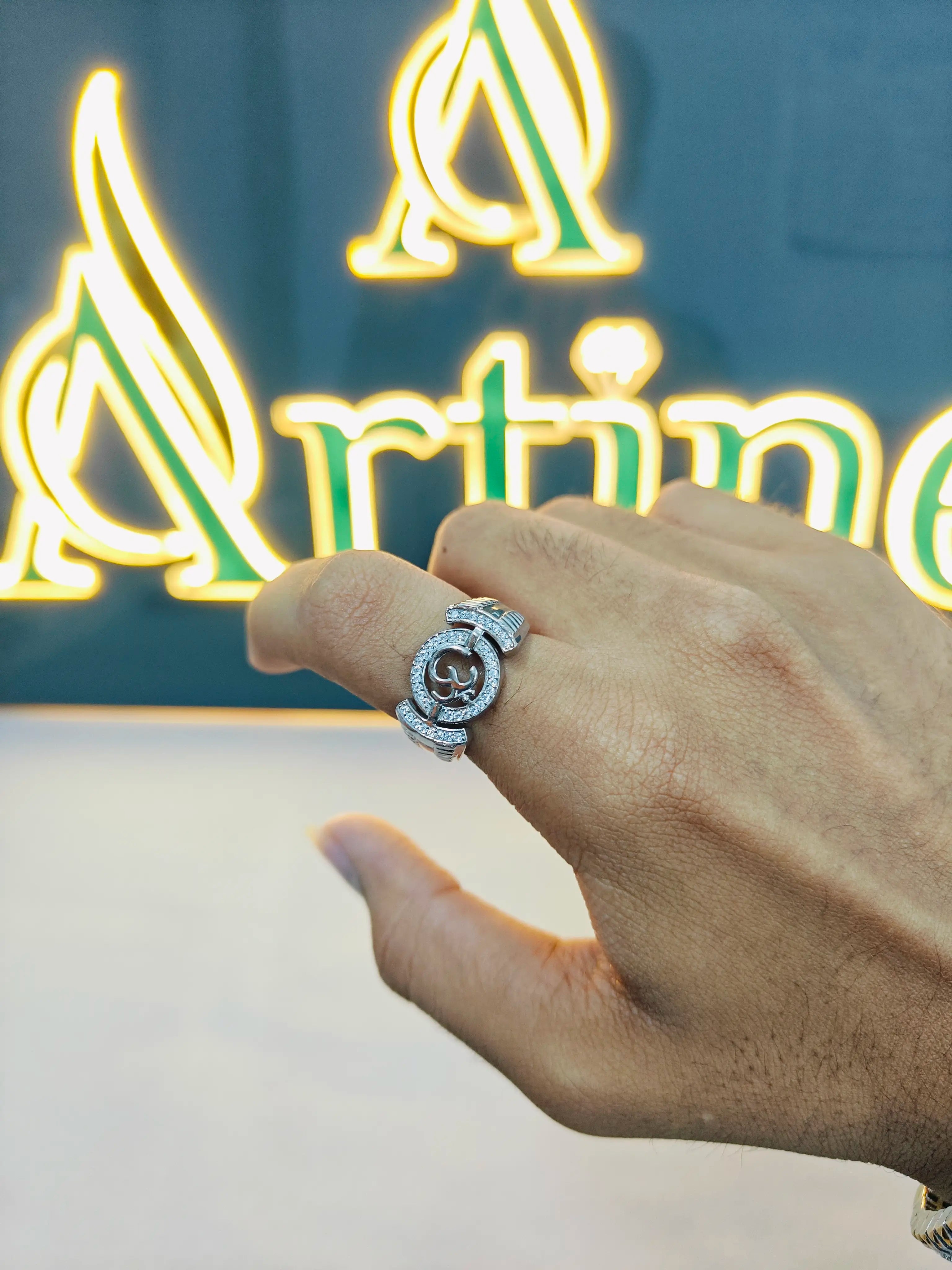 Hand wearing a silver ring with a visible brand logo in the background
