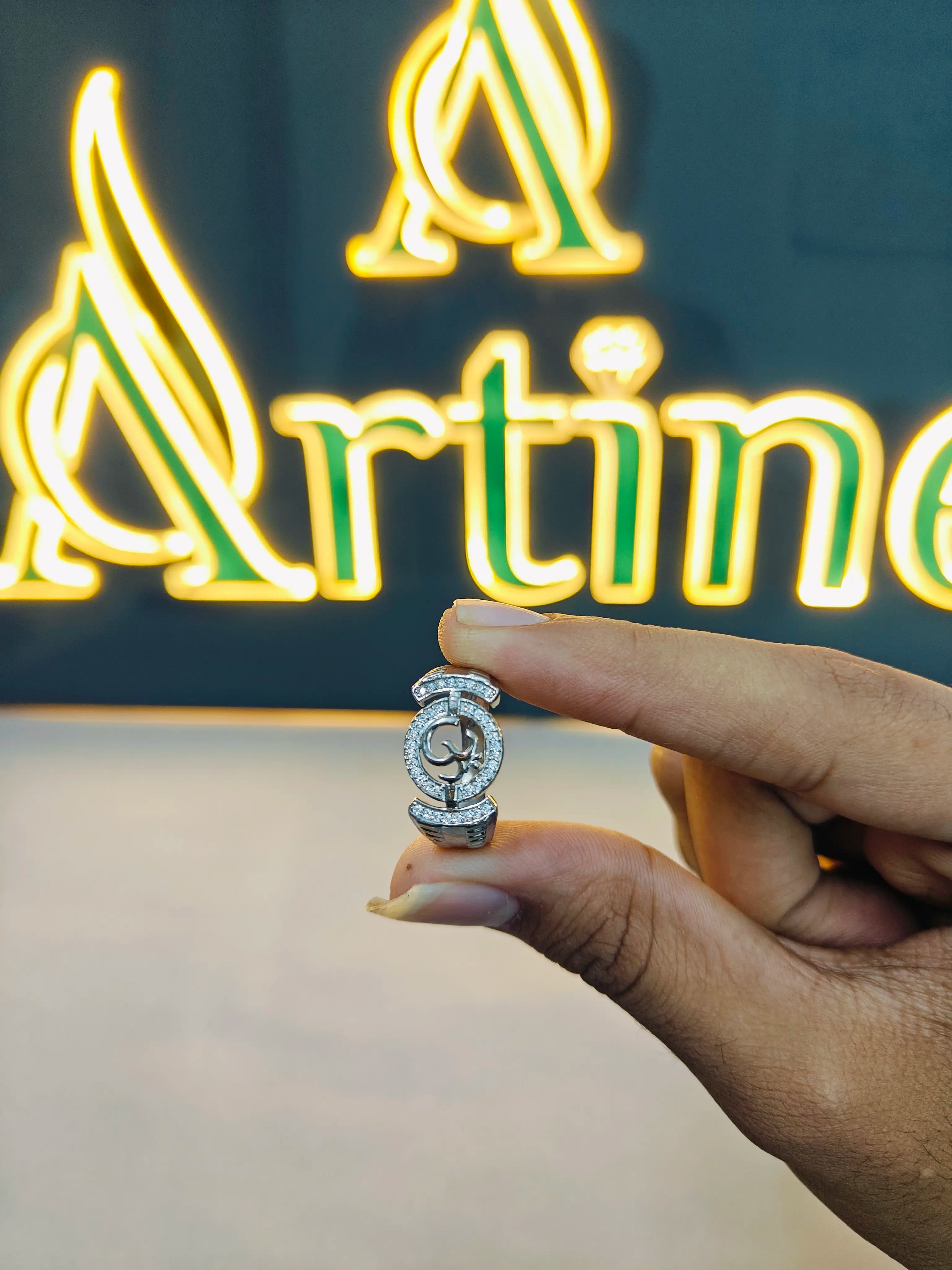 Hand holding a diamond ring in front of a neon sign with 'Artine' on a dark background