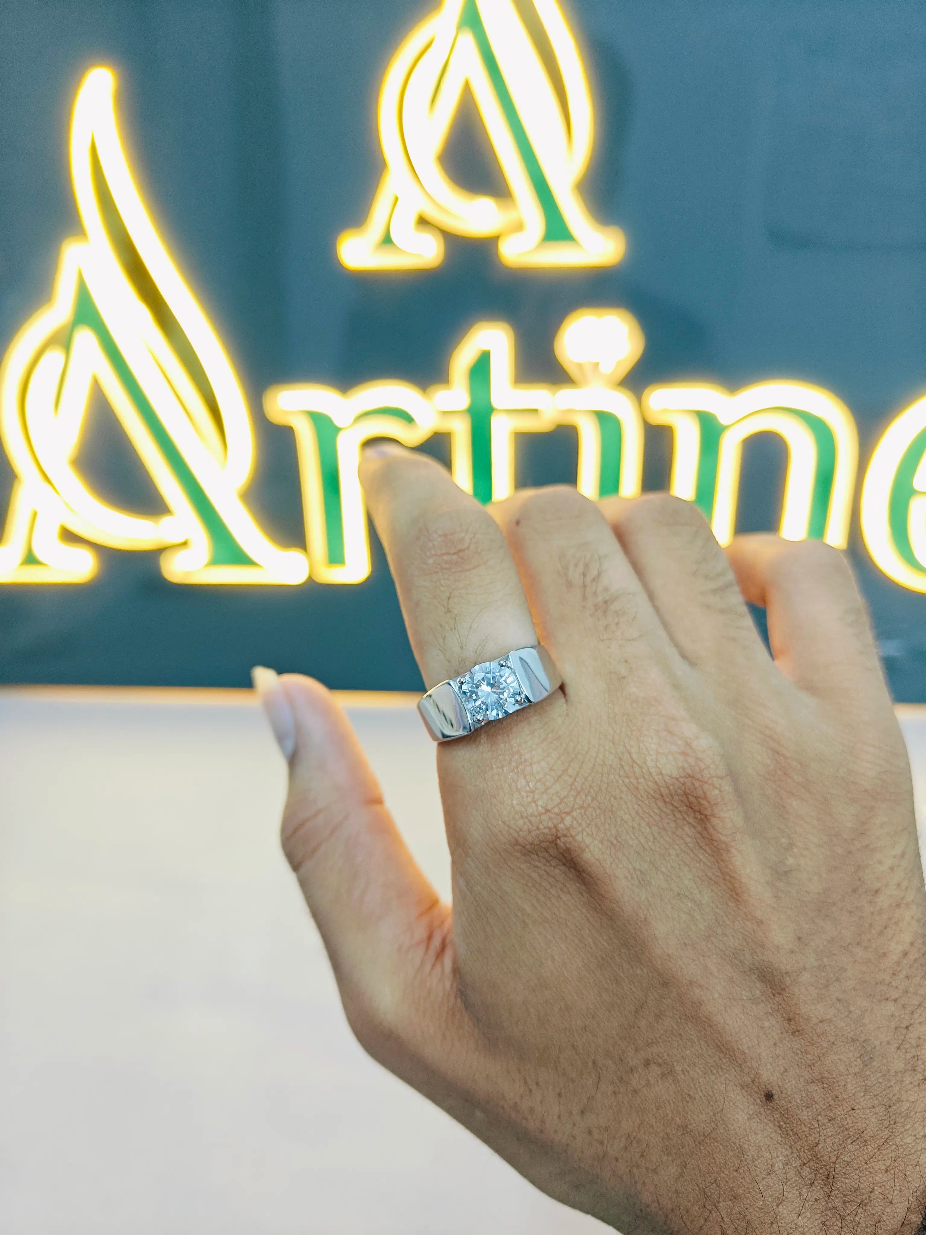 Hand wearing a diamond ring with a neon sign in the background