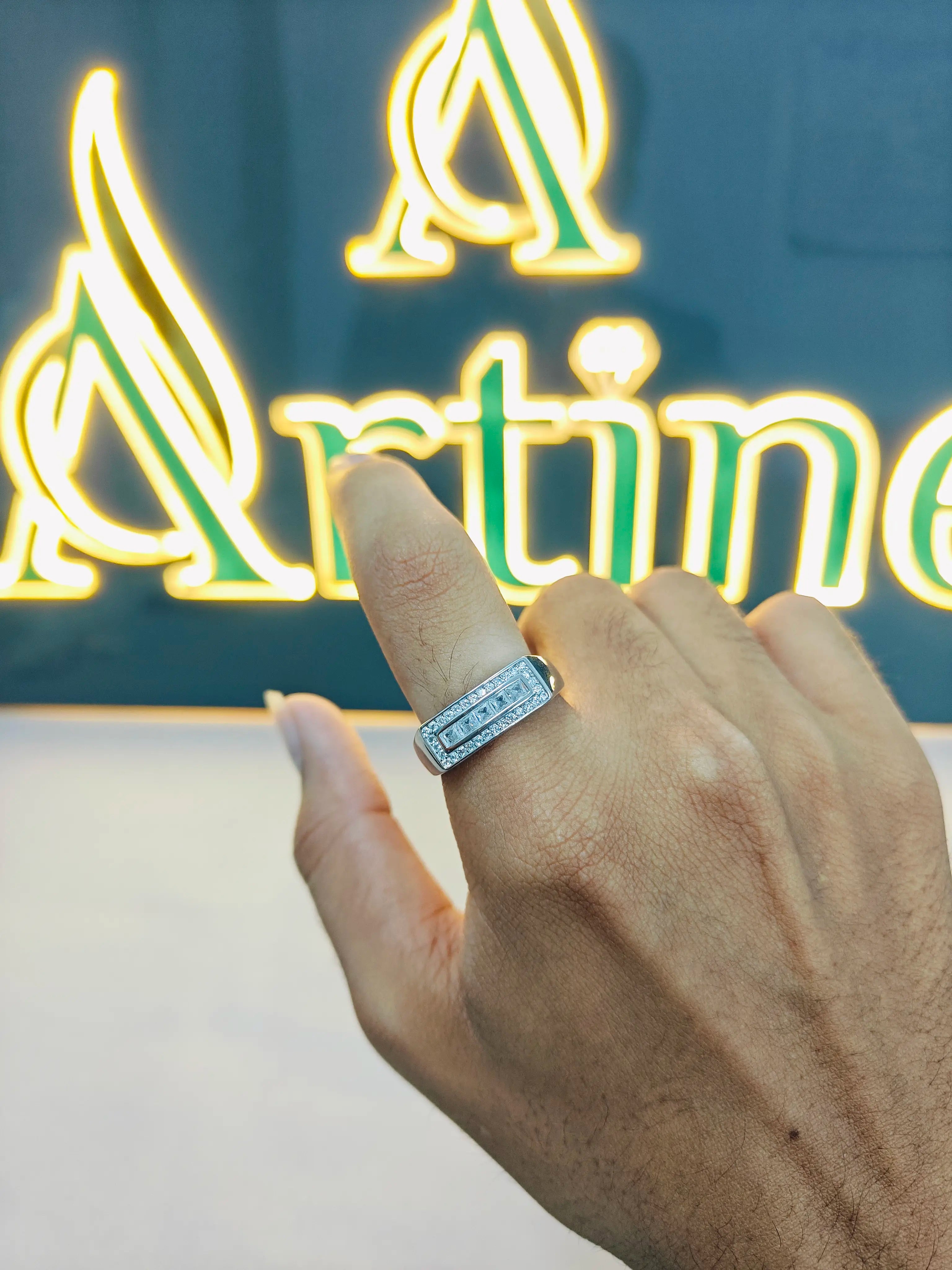 Hand wearing a diamond ring with a neon sign in the background