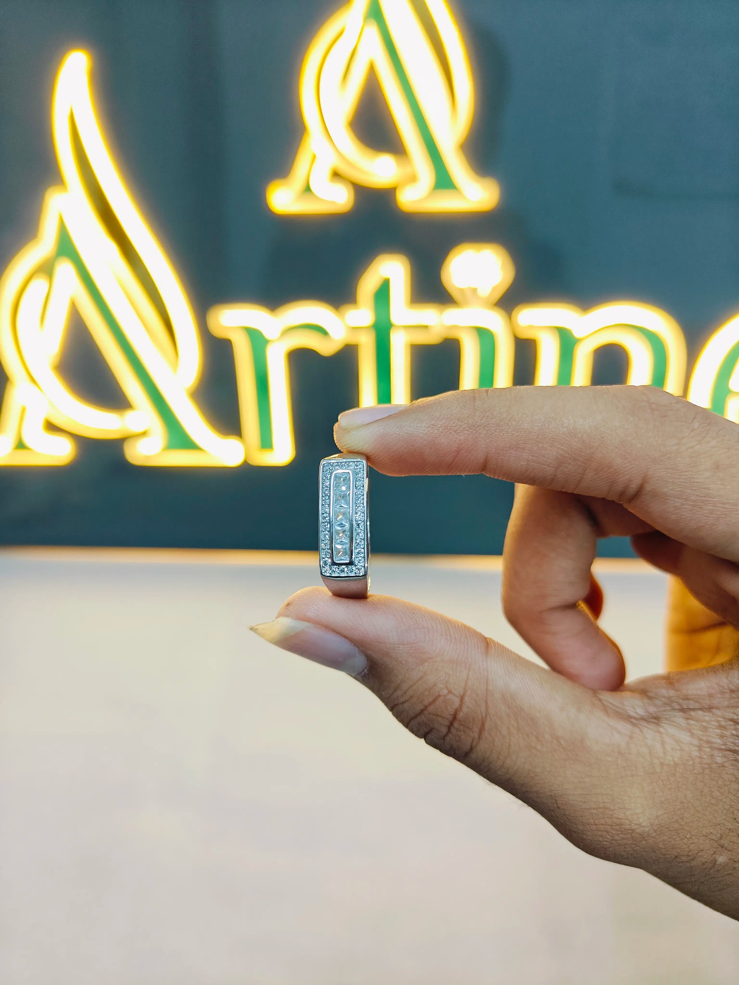 Hand holding a small rectangular object with a neon 'Artemis' sign in the background