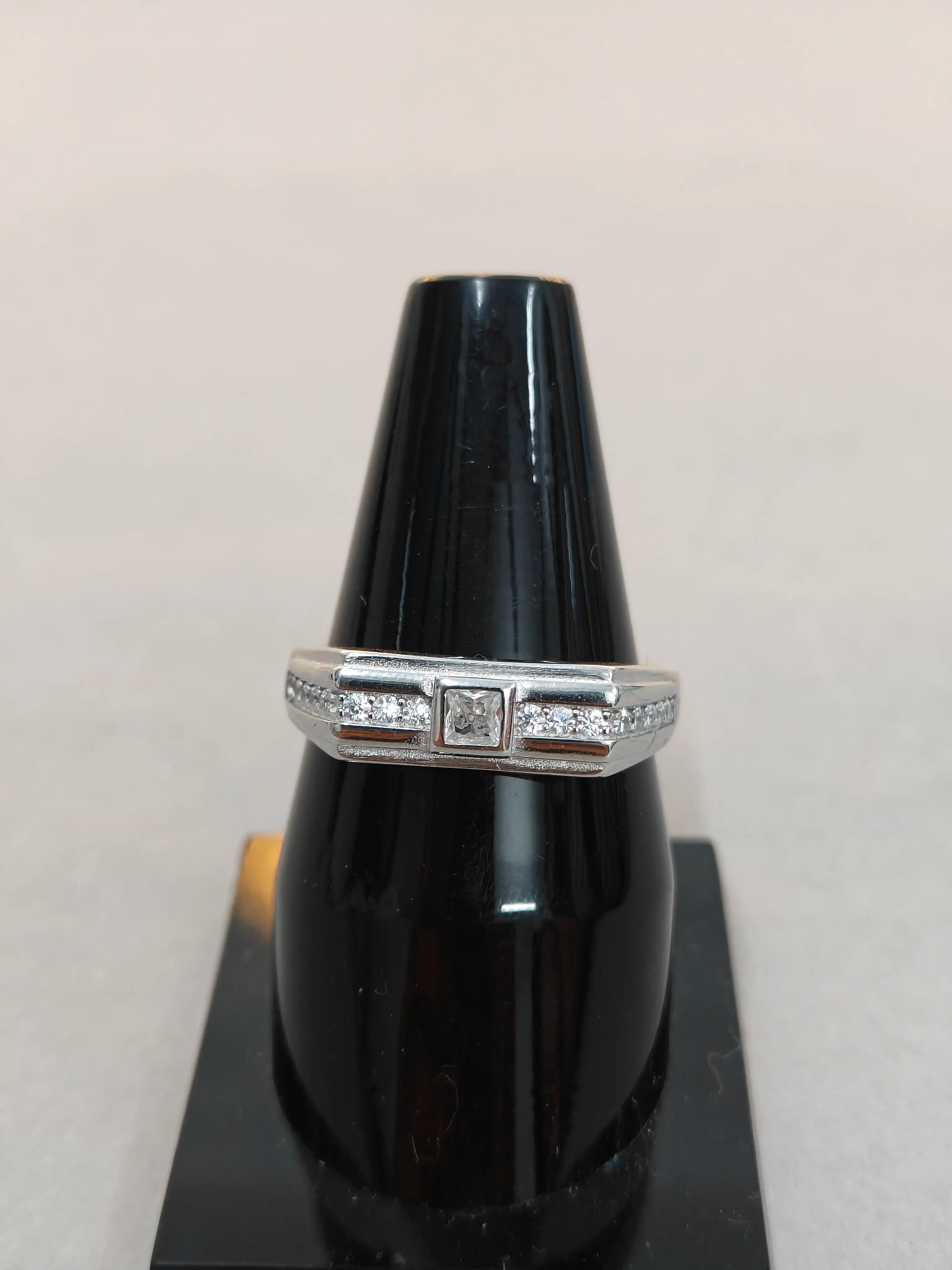 Silver ring with diamonds on a black stand against a light gray background