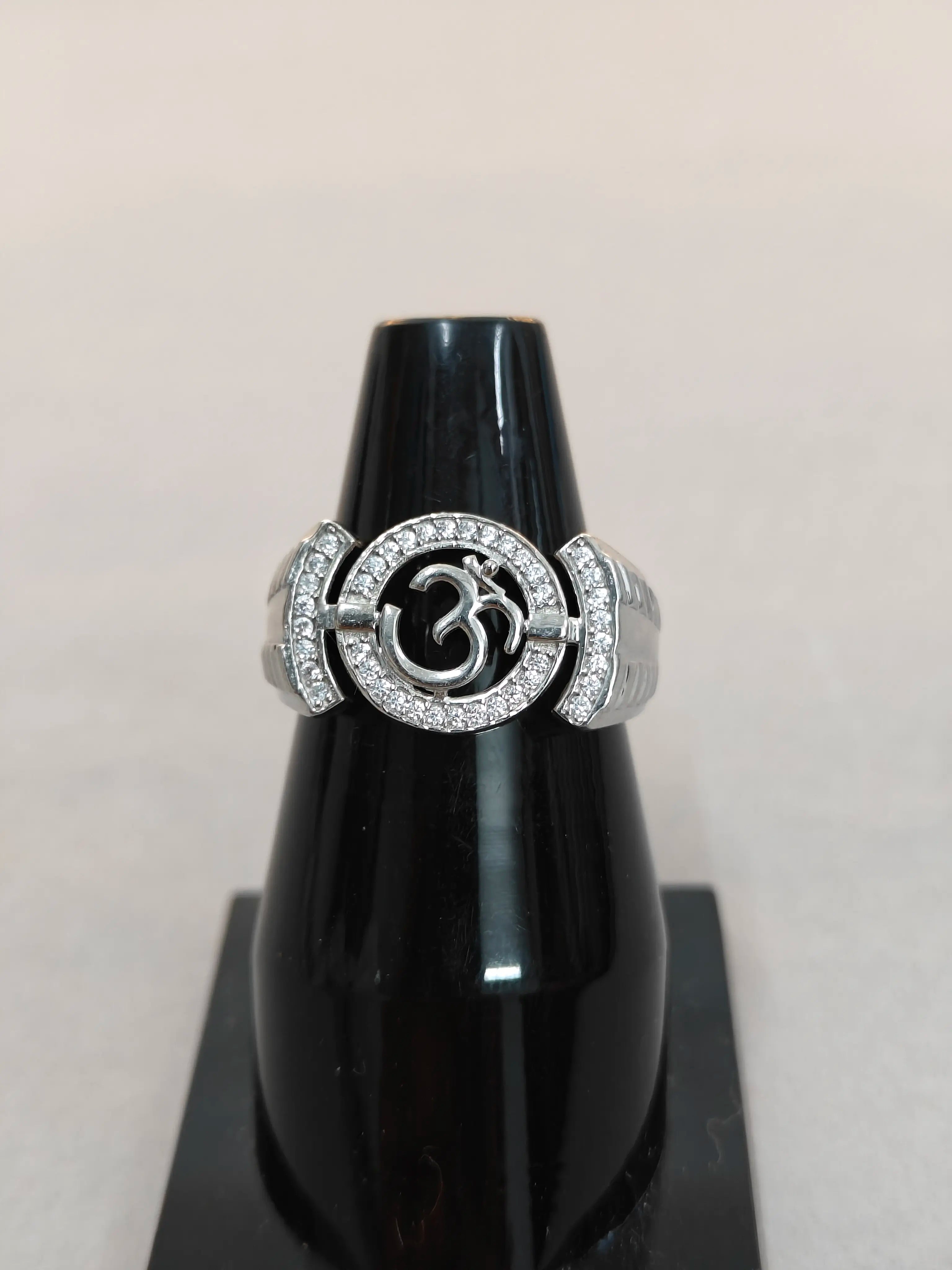 Silver ring with a circular design on a black stand against a light gray background